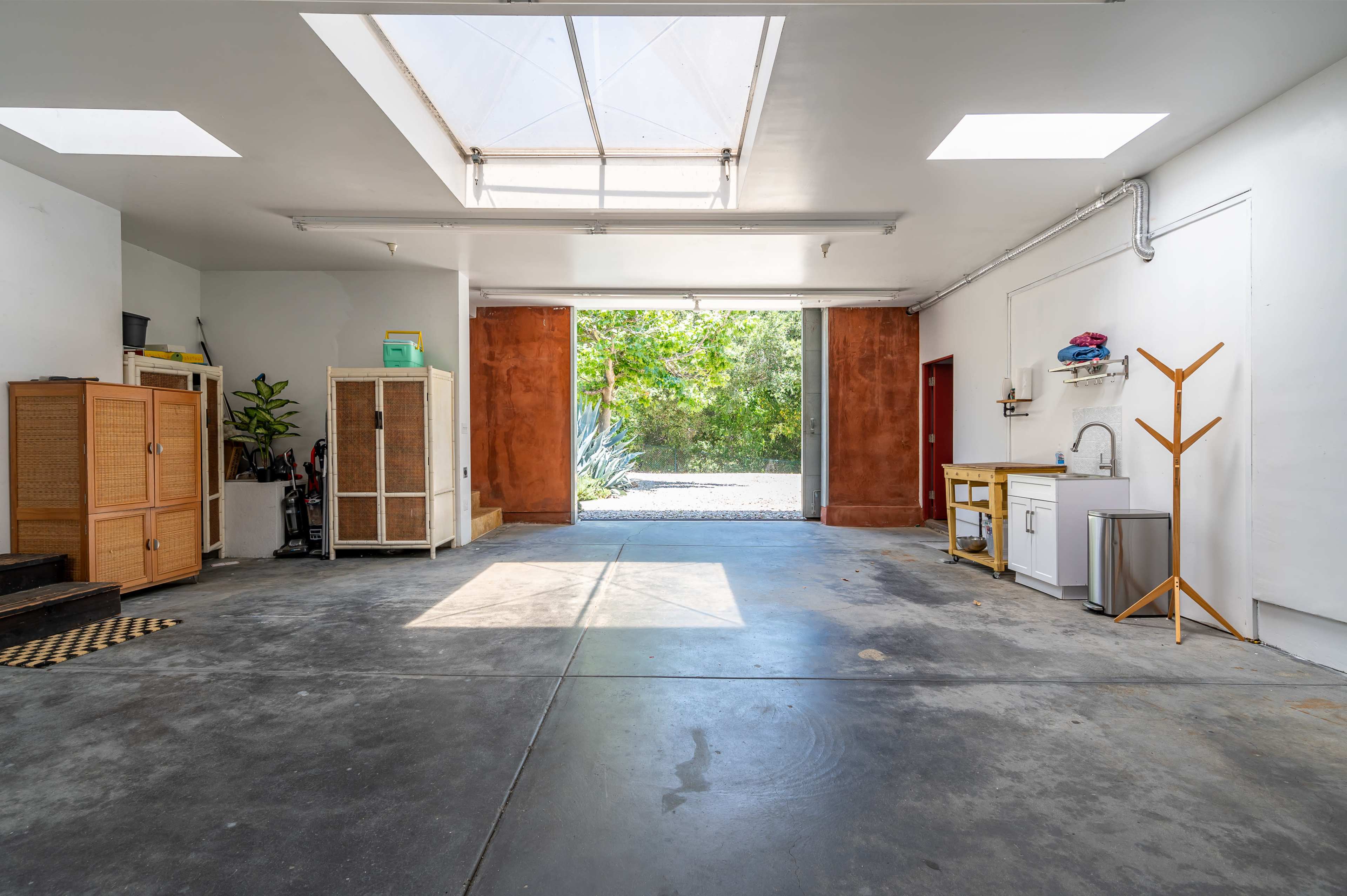 A spacious garage features a skylight, storage cabinets, and a clear view of greenery through an open door.