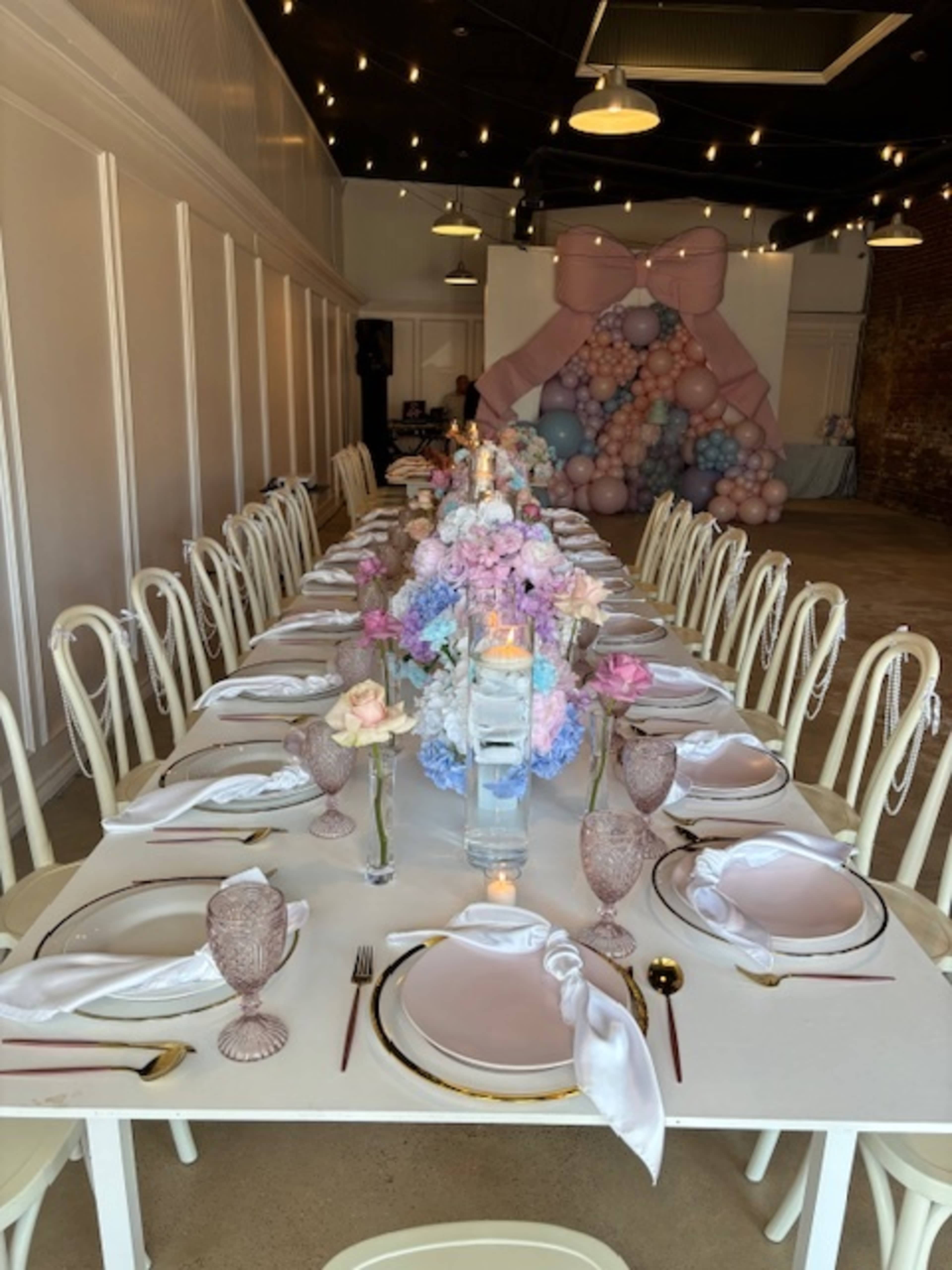 A long banquet table is elegantly set with floral centerpieces and pastel-colored decorations in a spacious indoor venue.