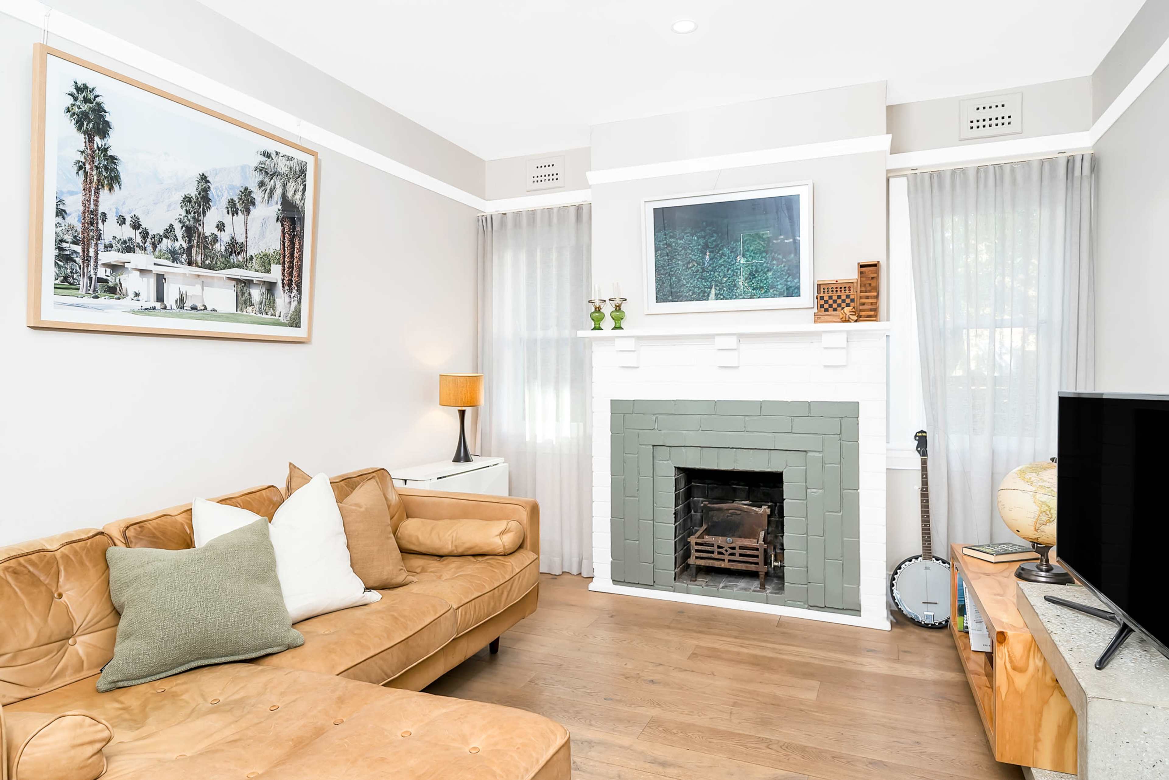 A living room with a tan sectional sofa, a fireplace with a green facade, framed artwork on the wall, and a banjo next to a TV.