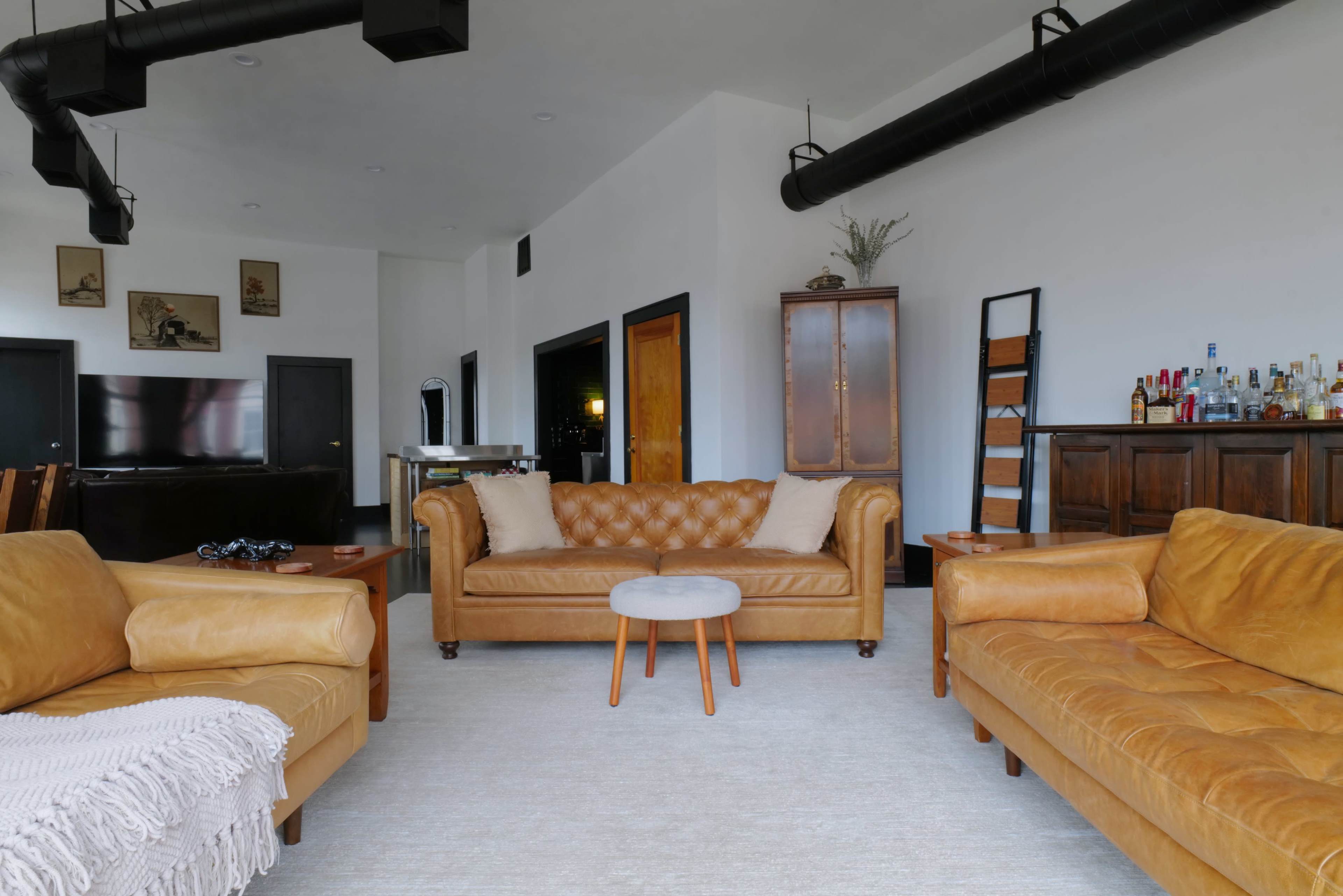 The image shows a modern living room featuring two leather sofas, a small round table, and a bar area in the background.