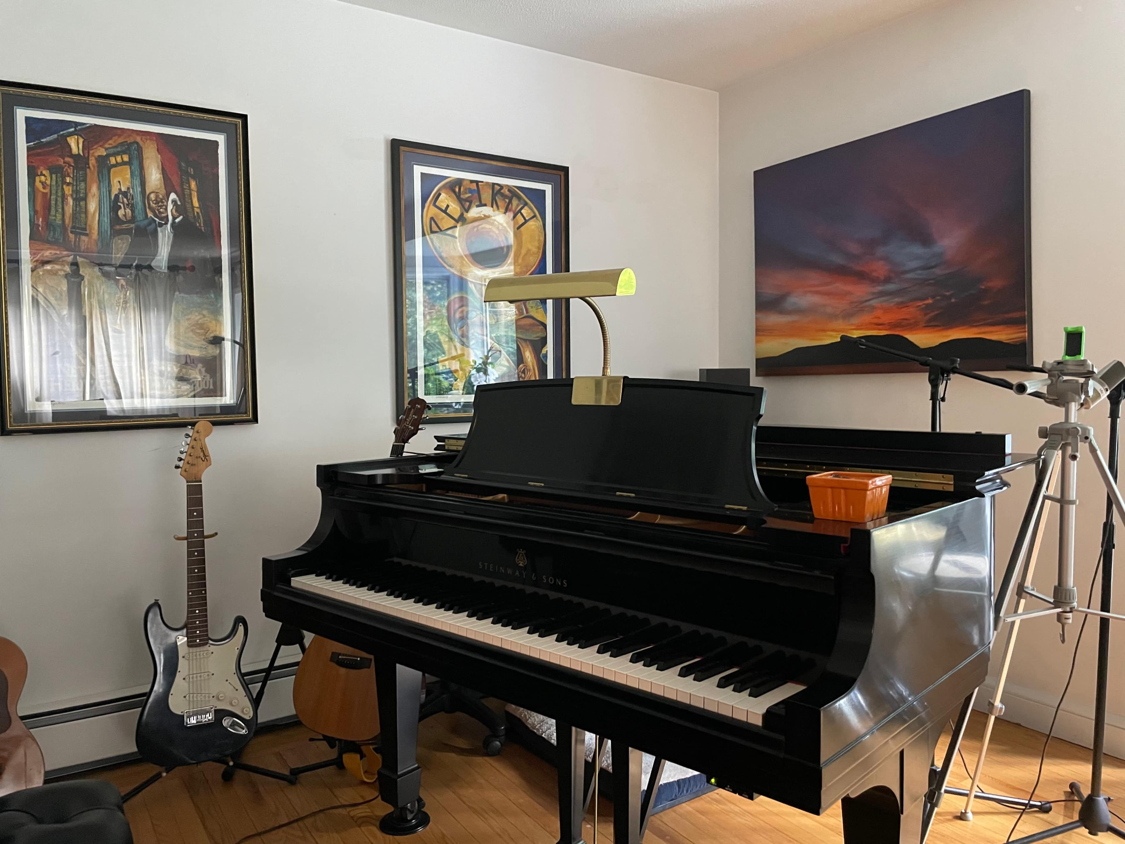 A grand piano sits in a room decorated with framed artwork, alongside various musical instruments and equipment.