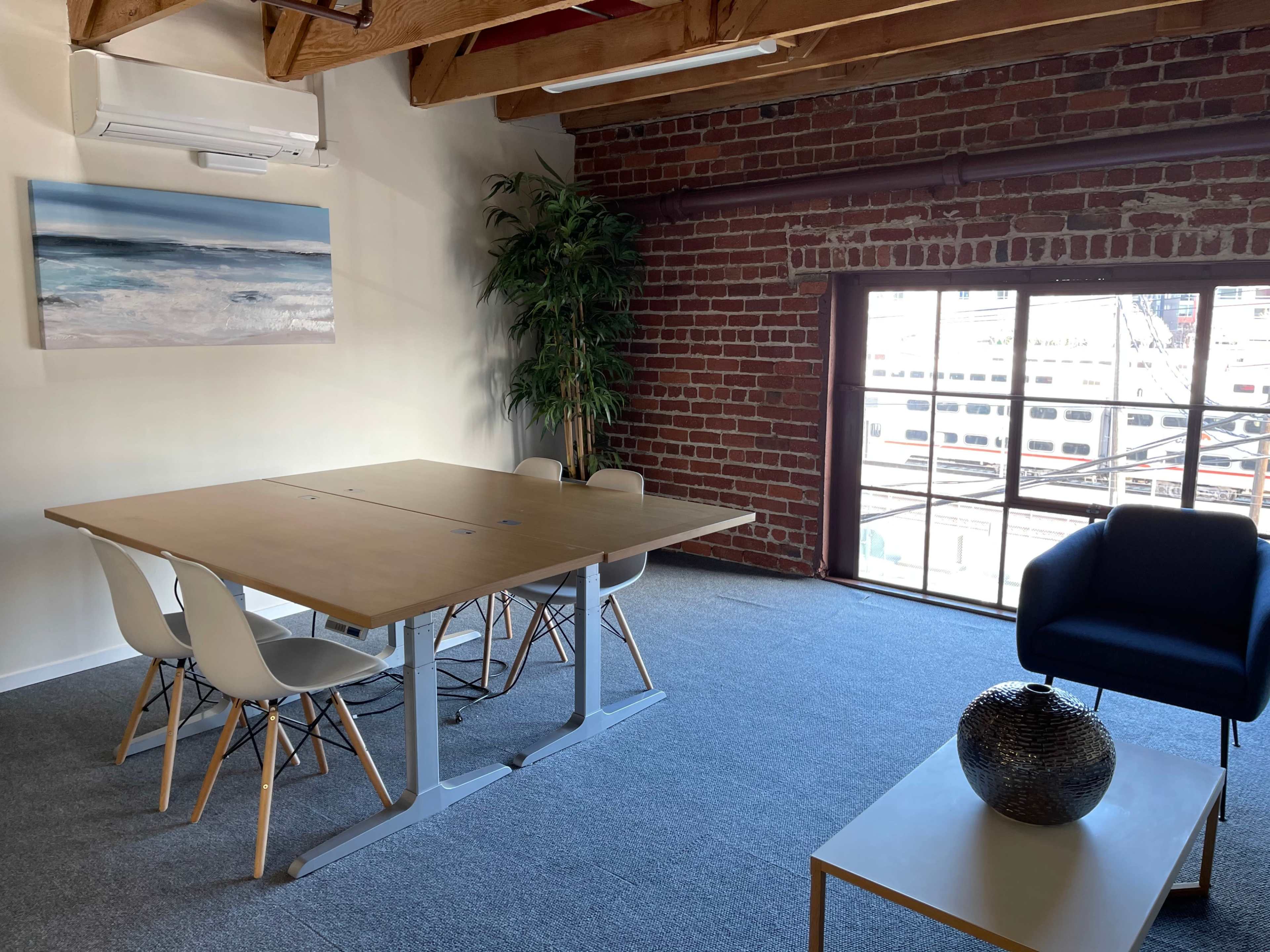 A modern workspace featuring a wooden table surrounded by four white chairs, a blue armchair, and a large window with a view of an outdoor harbor.