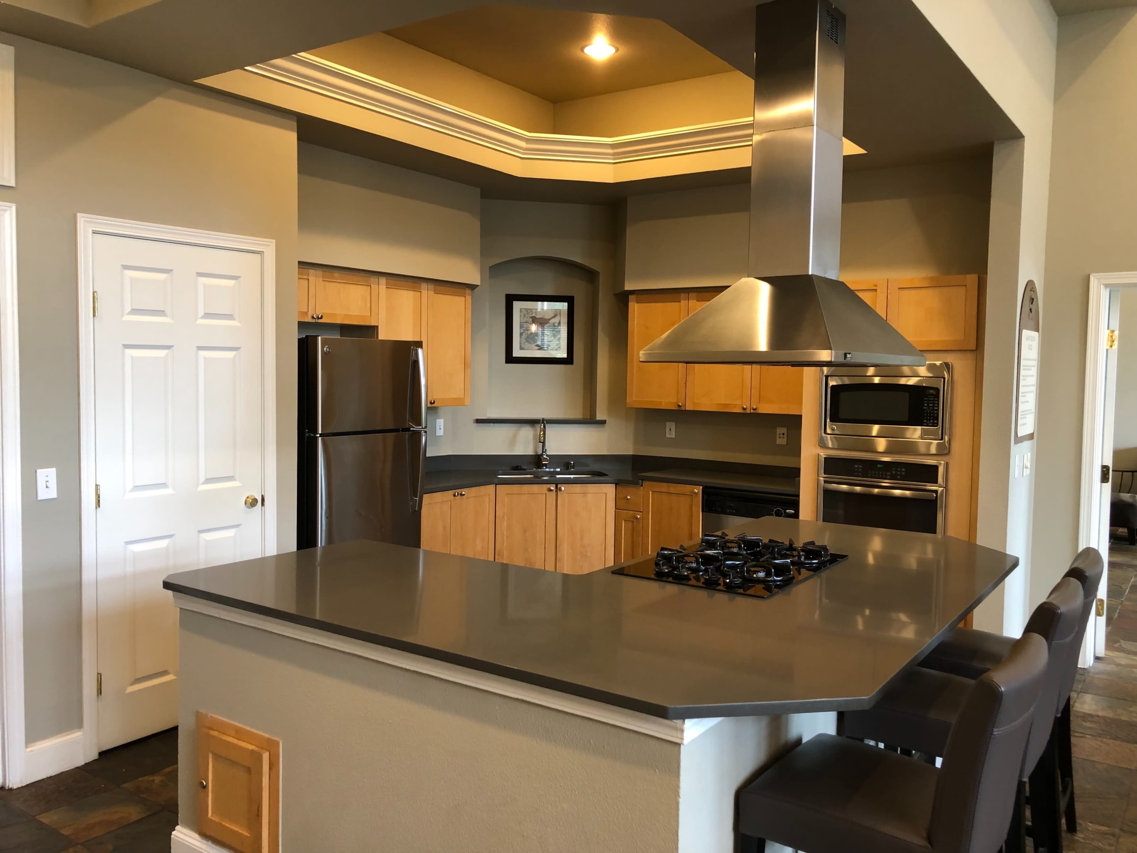 The image shows a modern kitchen with wooden cabinets, stainless steel appliances, and a gray countertop with a built-in gas stove.