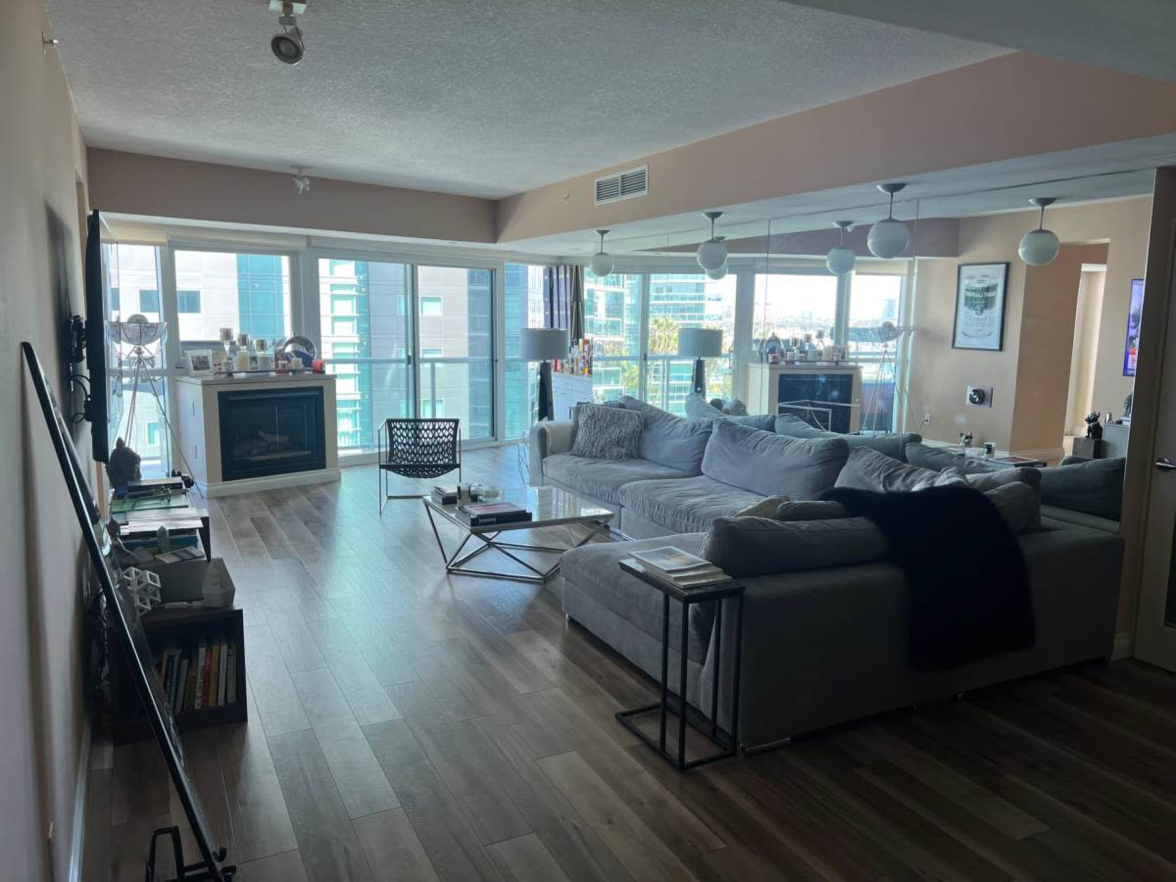 A modern living room with a large sectional sofa, a coffee table, and a wall-mounted television, featuring large windows that provide natural light.
