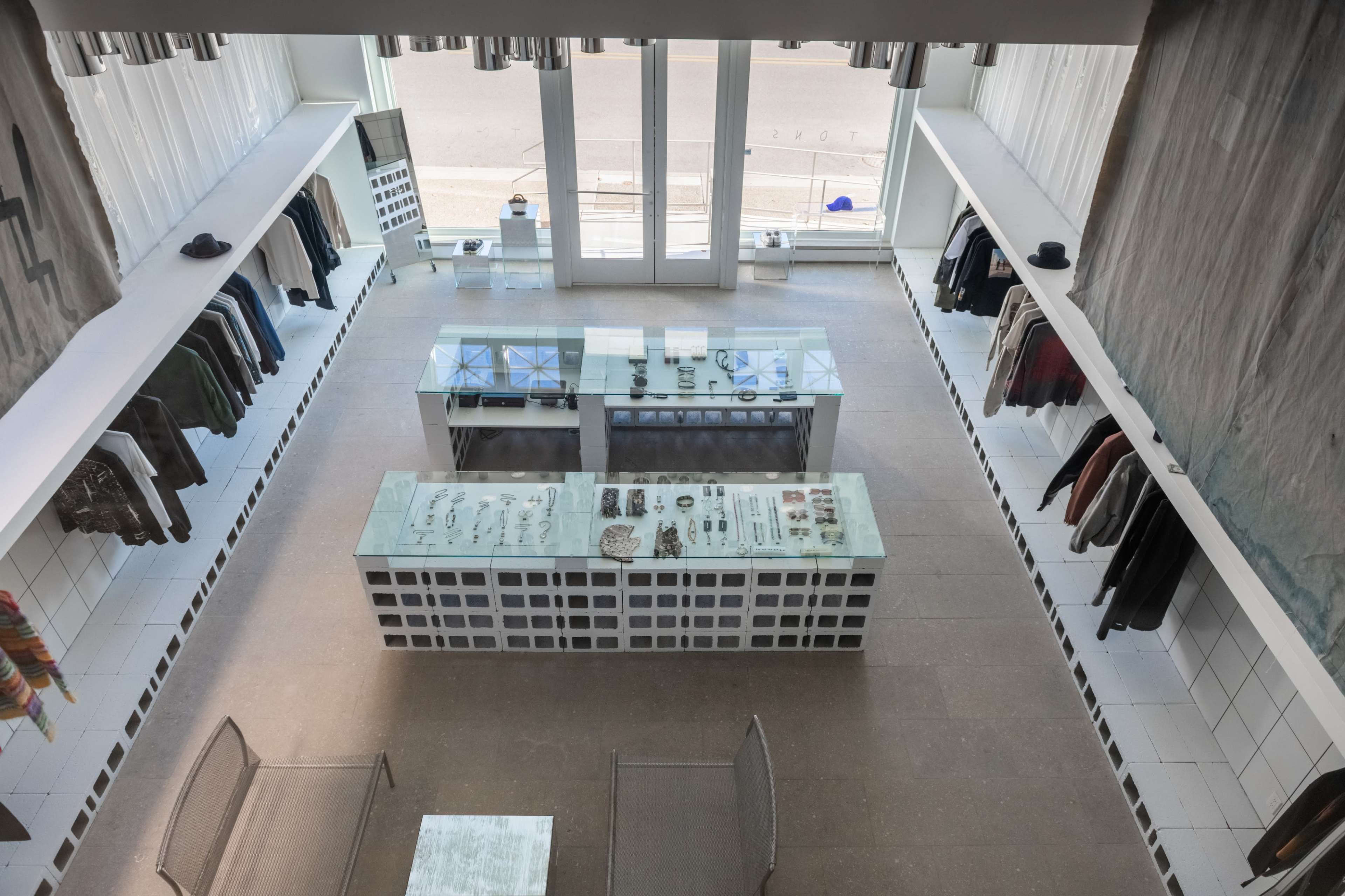 The image shows a modern retail space with clothing displayed on the walls and an island featuring various accessories and jewelry in the center.