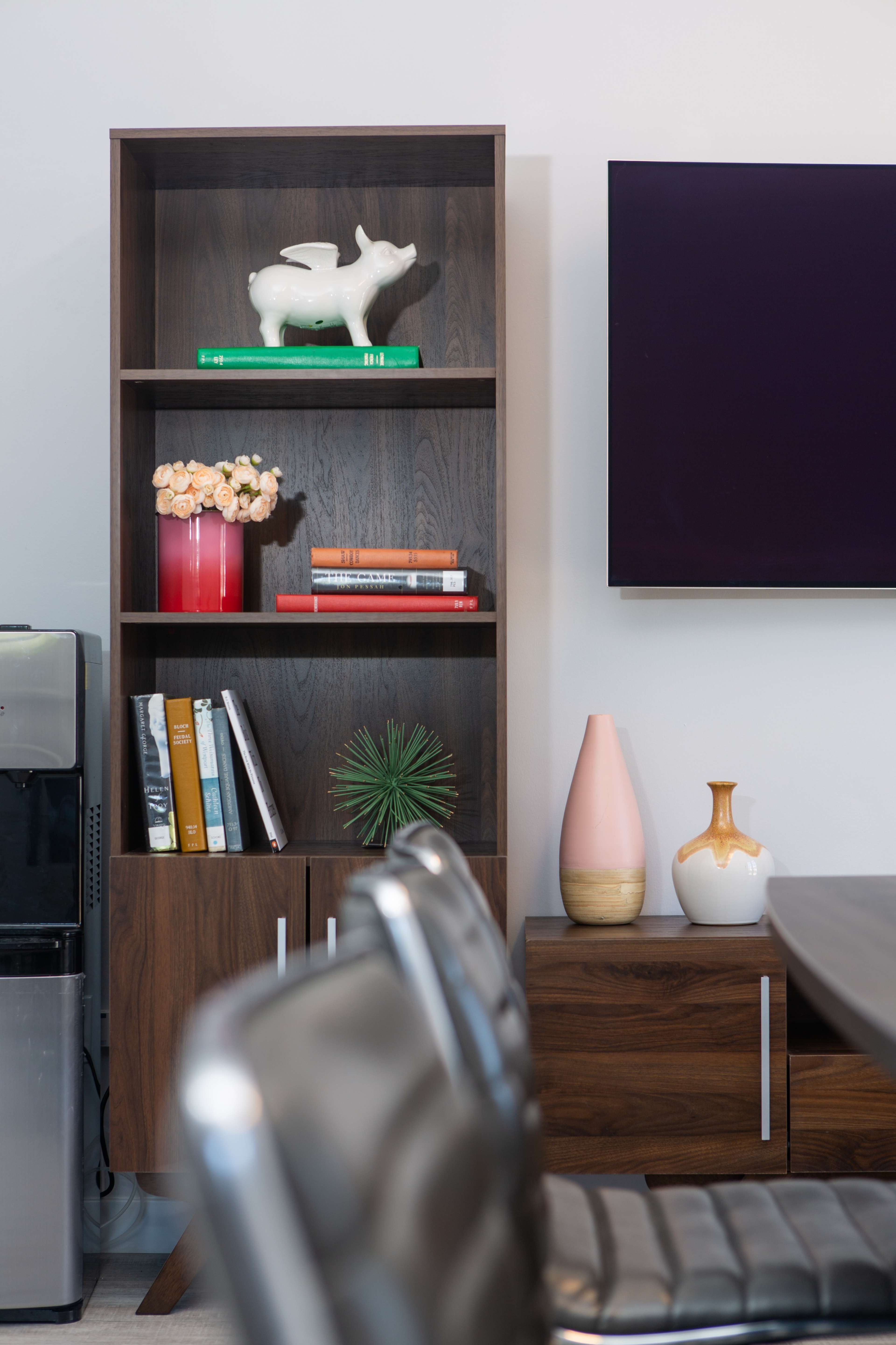 A modern shelving unit displays decorative items and books next to a sleek dining table and a television mounted on the wall.