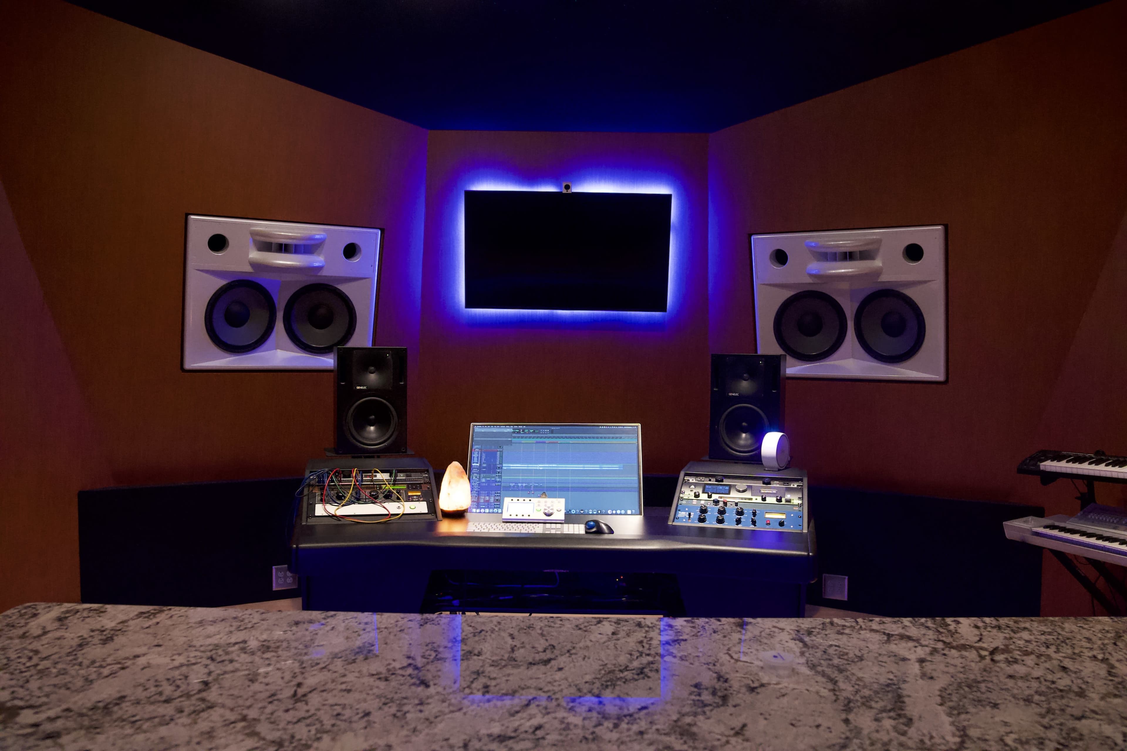 A modern music studio features a desk with a computer, various audio equipment, and large speakers, set against a backdrop with ambient lighting.
