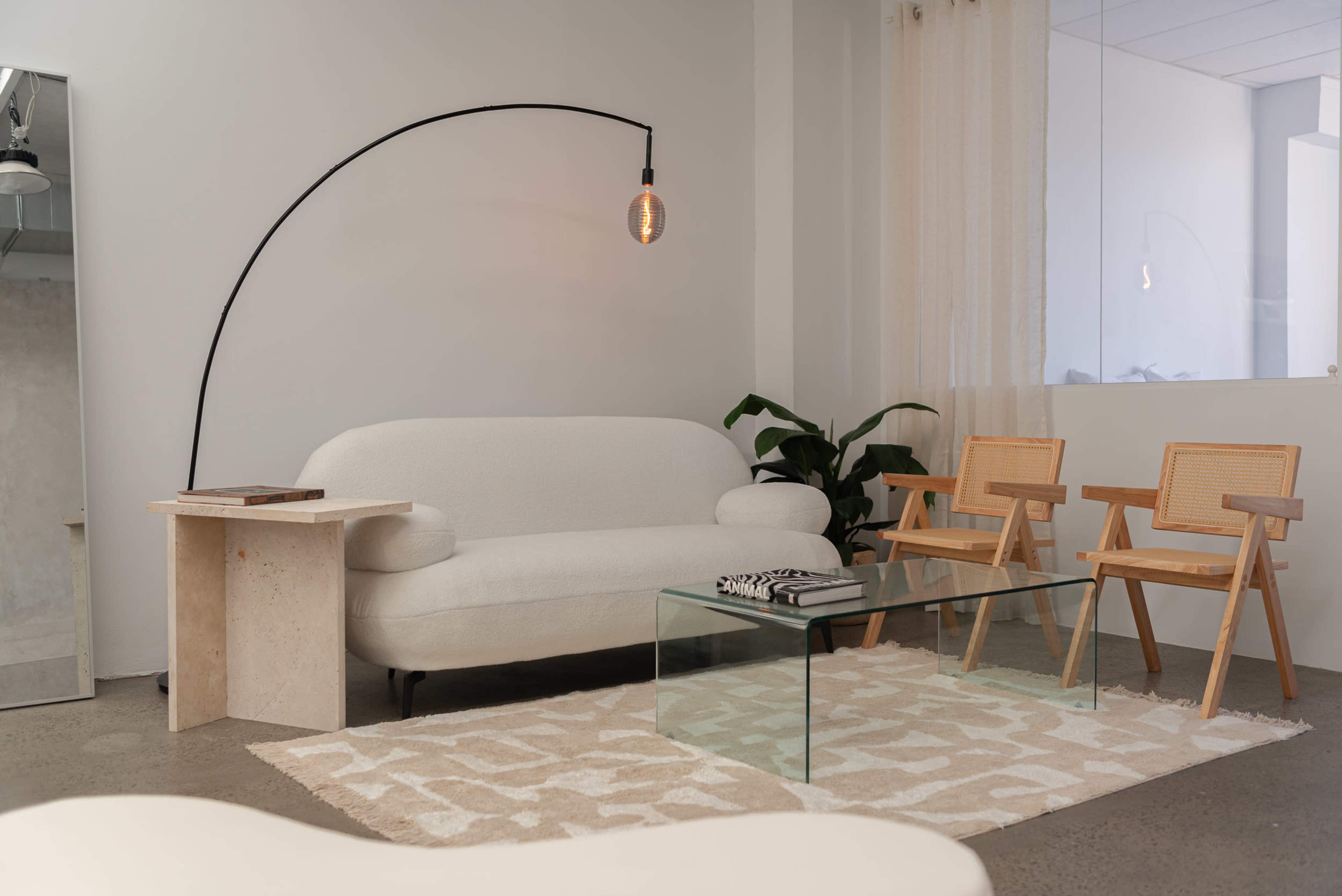A minimalist living room featuring a white upholstered sofa, two wooden chairs, a glass coffee table, and a small side table beside the sofa.