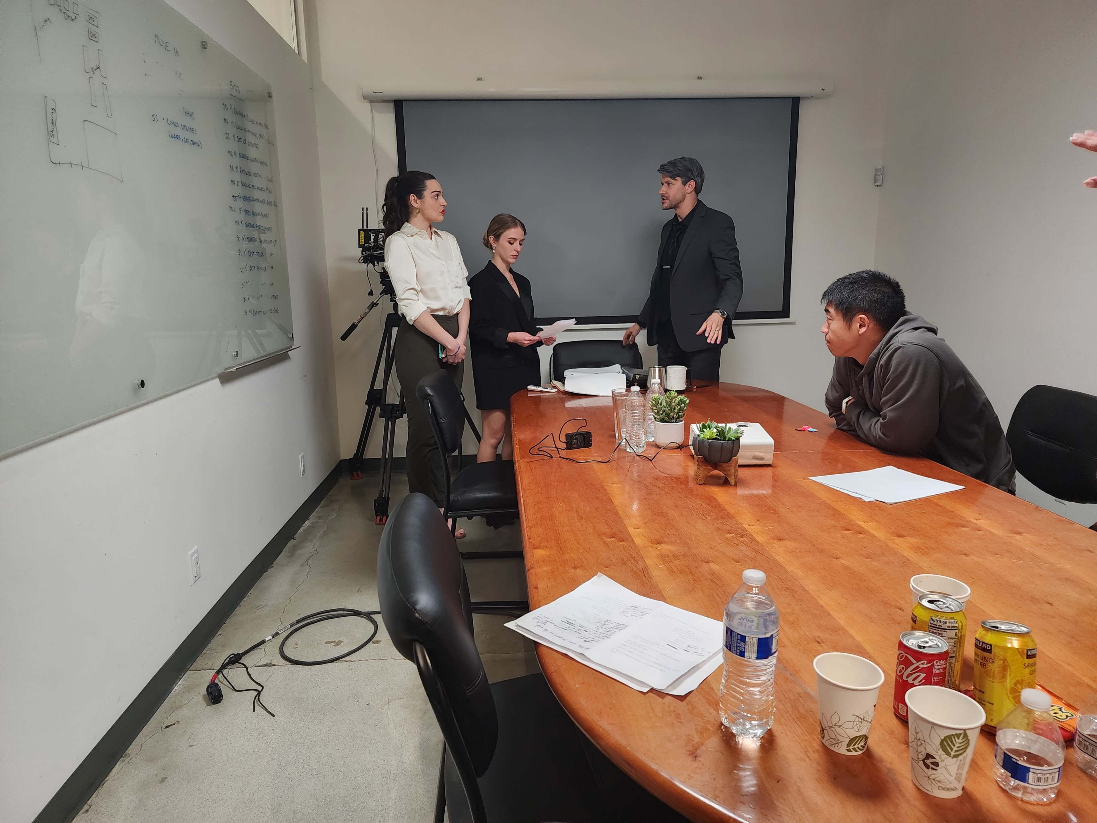A group of four individuals engage in a discussion around a large wooden conference table in a meeting room.