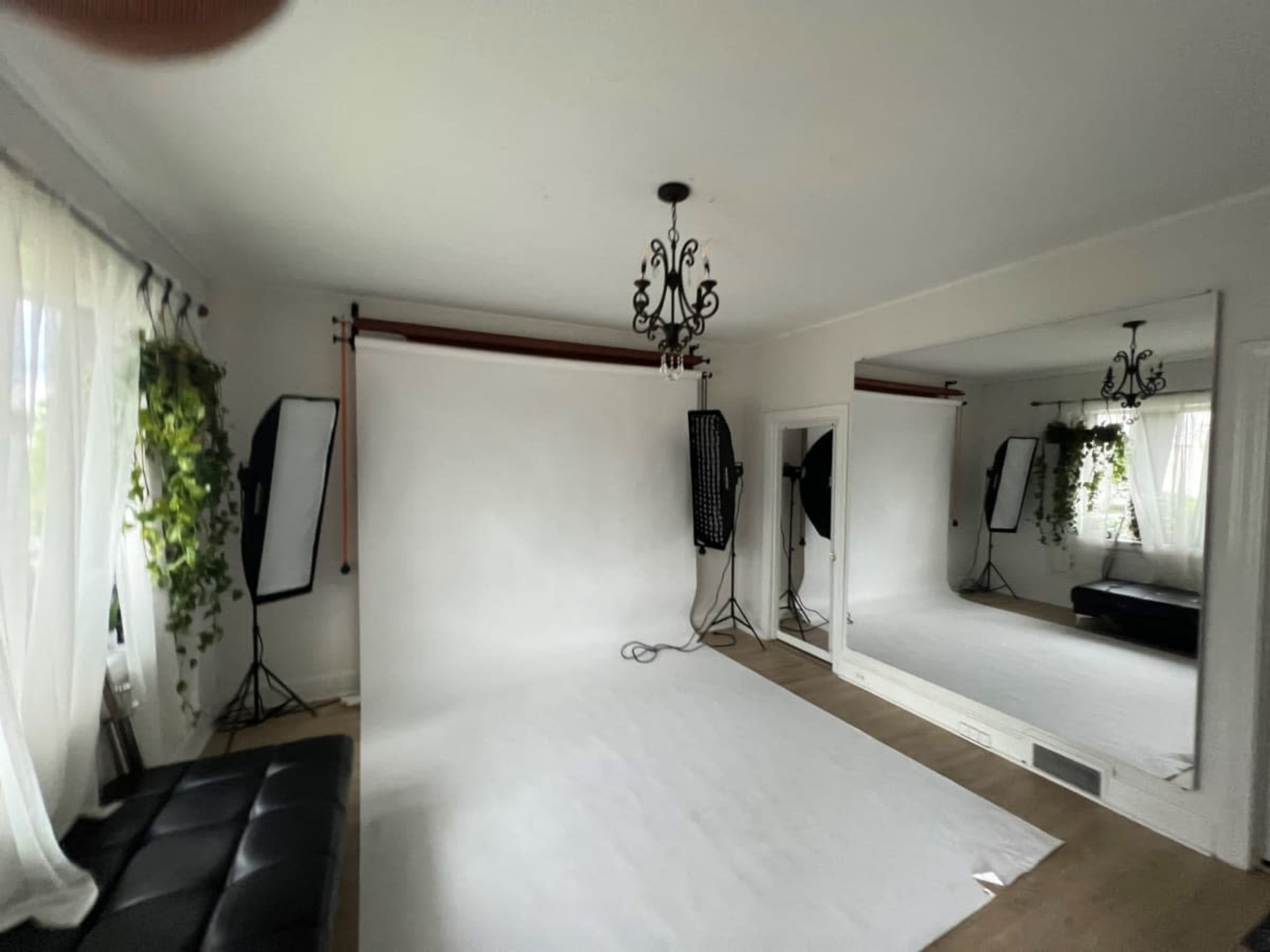 A well-lit studio space features a white backdrop, two softbox lights, a large mirror, and a black sofa.