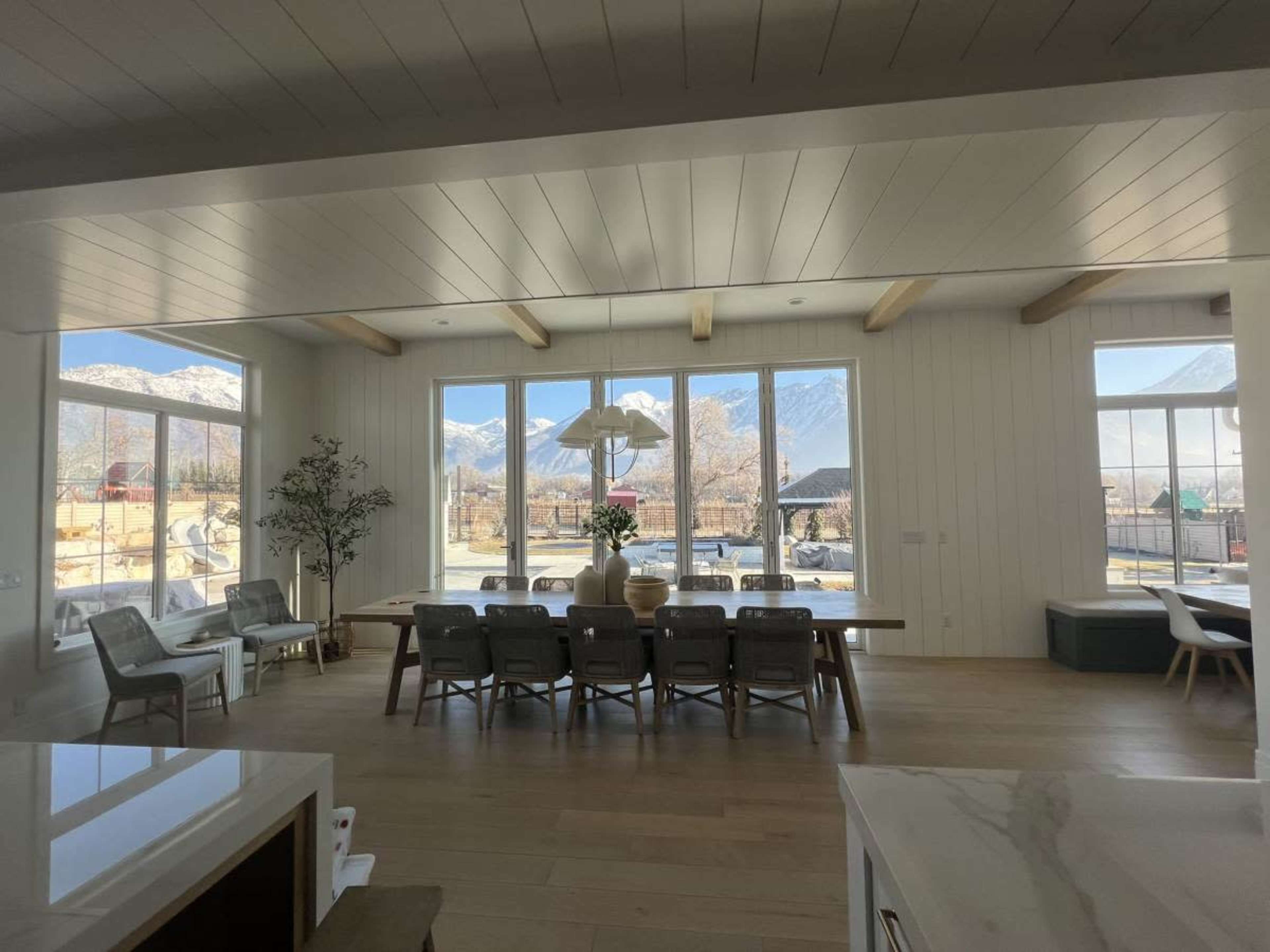 A modern dining area with large windows revealing a mountain view, featuring a long table and several chairs.