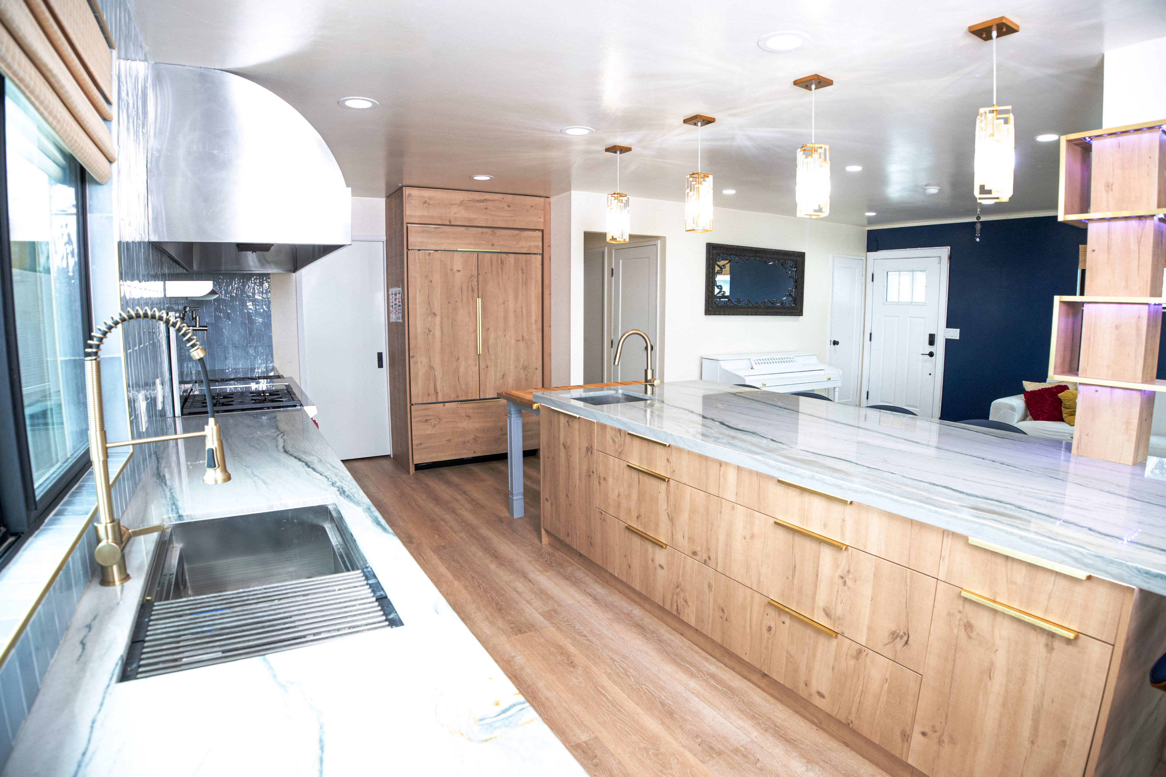 The image shows a modern kitchen with wooden cabinetry, a large island with a marble countertop, and stainless steel appliances.