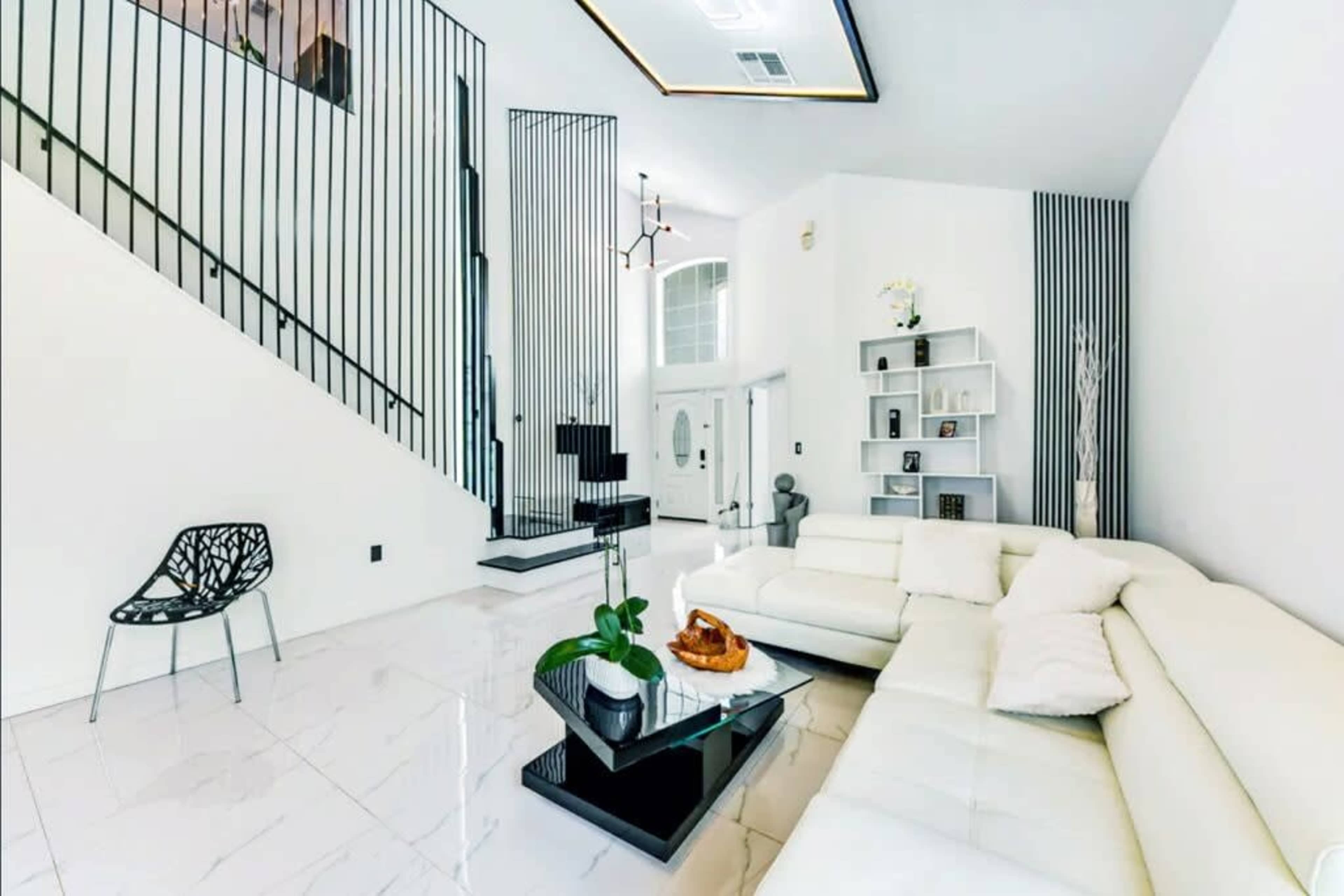A modern living room with a white sectional sofa, a black coffee table, and a staircase with a black railing leading to an upper level.