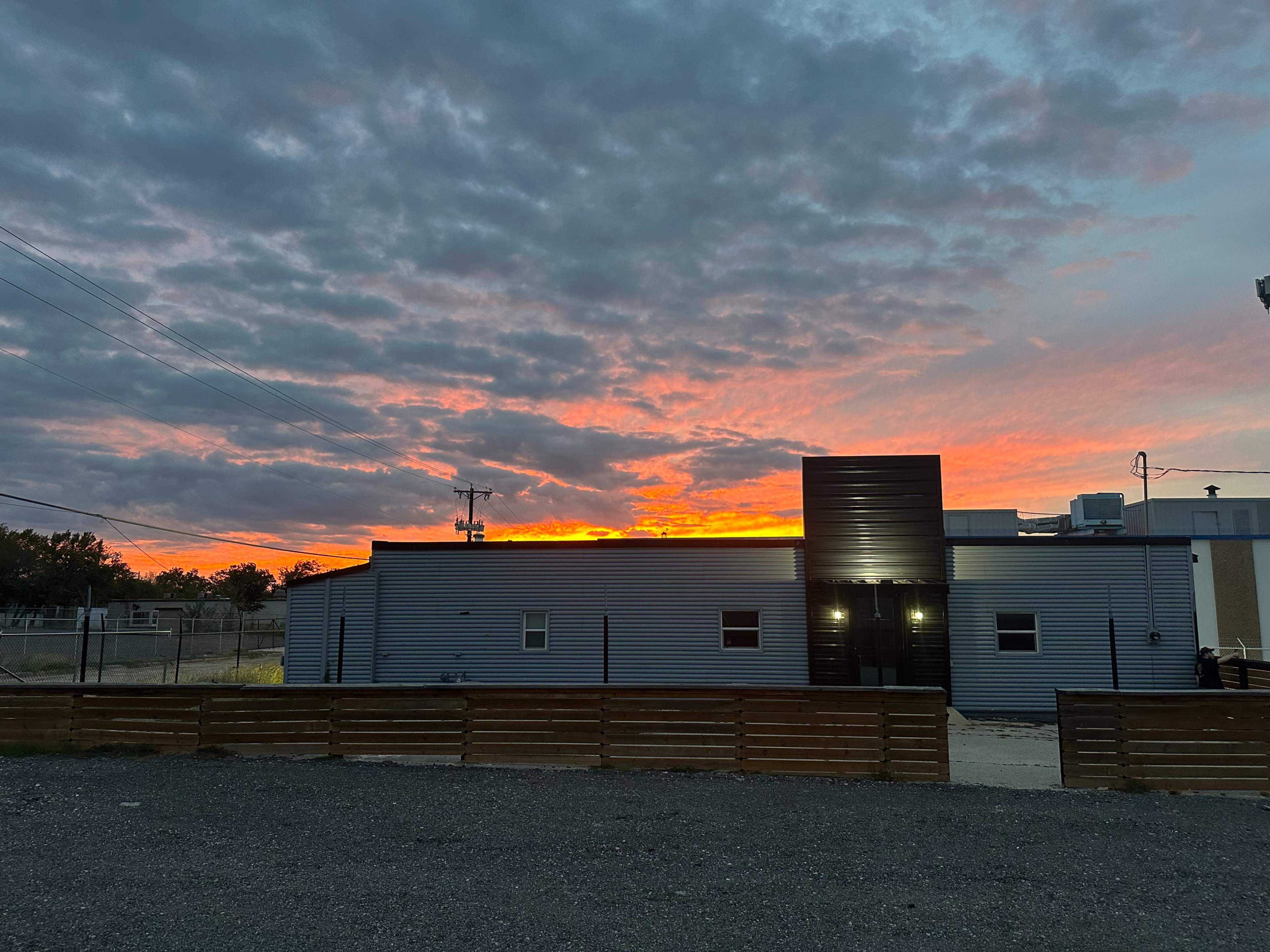 A gray building with a black section stands against a vibrant sunset sky filled with clouds.