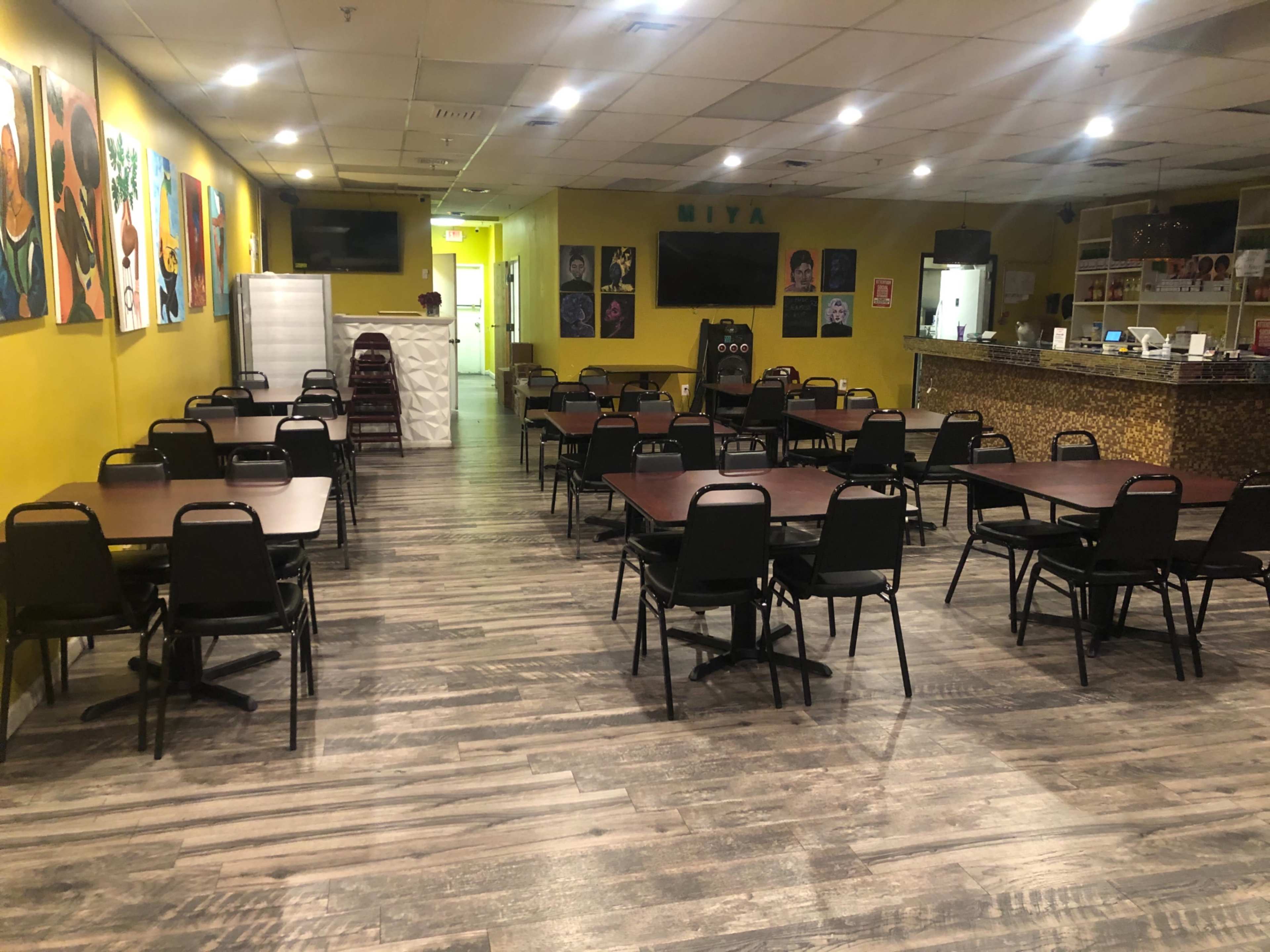 A spacious dining area with multiple tables and chairs, bright yellow walls, and artwork hanging on the walls.