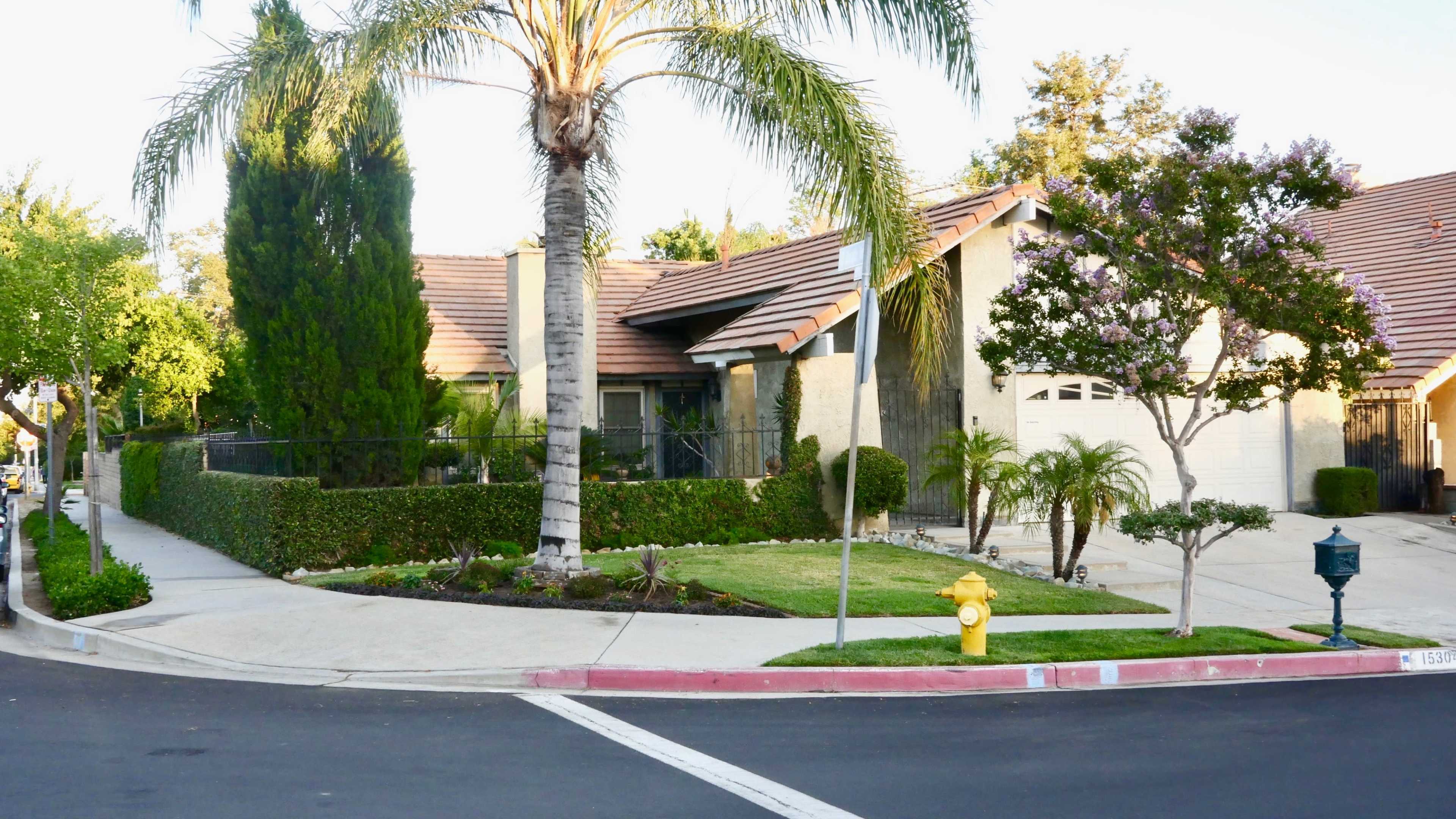 A suburban house with a landscaped yard, palm trees, and a driveway on a corner lot.