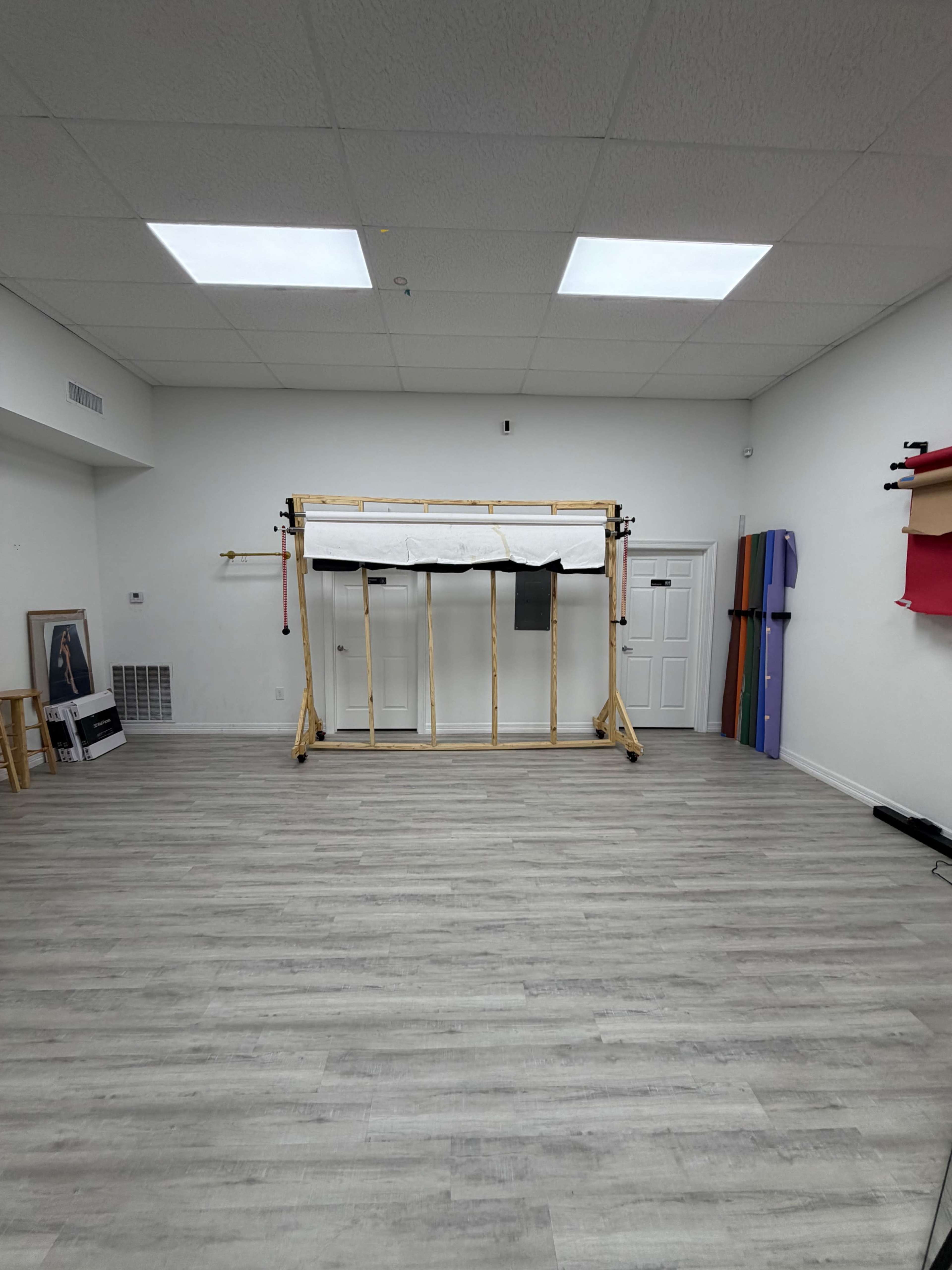 The image shows a spacious, empty studio with wooden structures in the center and various colored mats leaning against the wall.