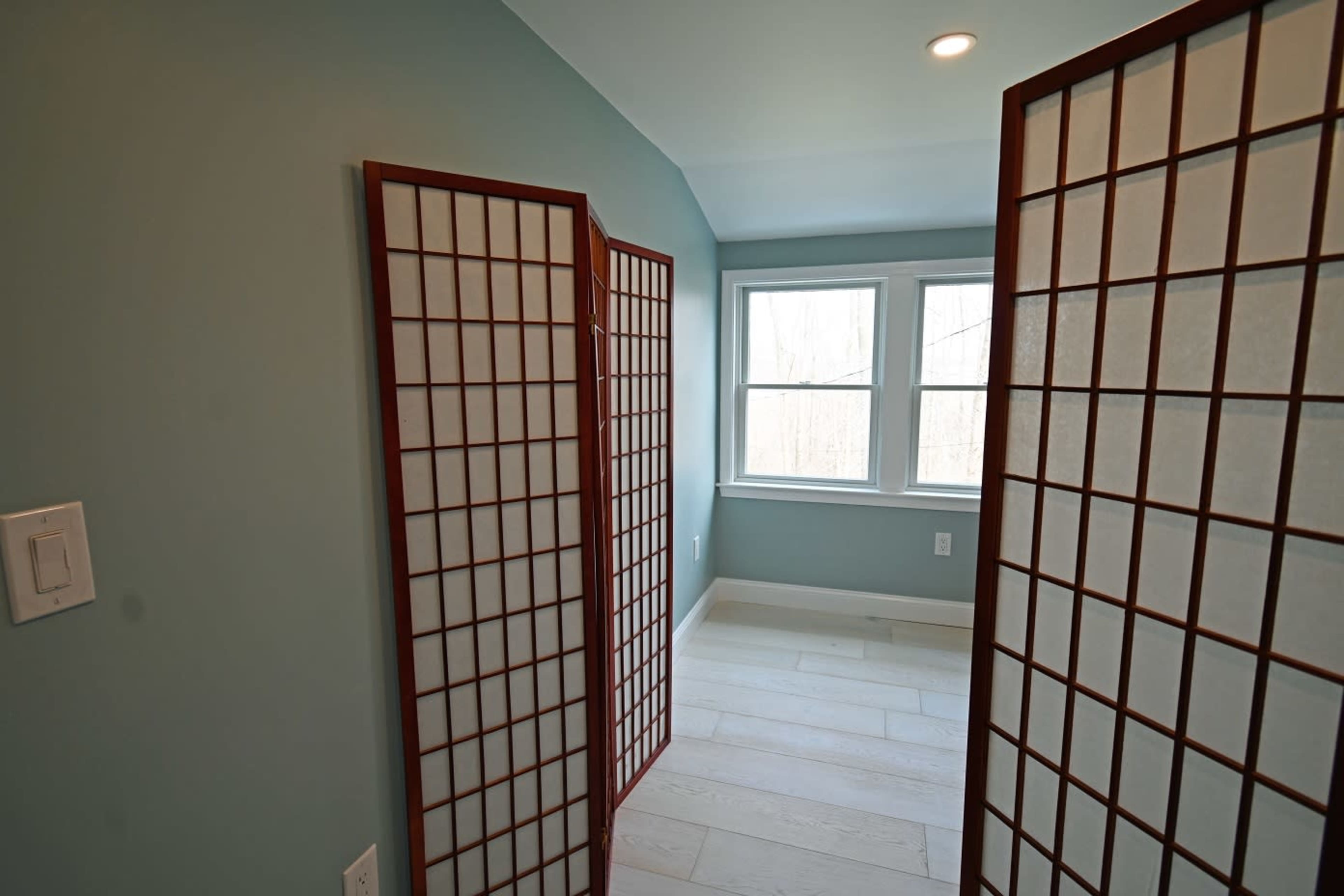 A light-colored room separated by wooden folding screens, with large windows letting in natural light.