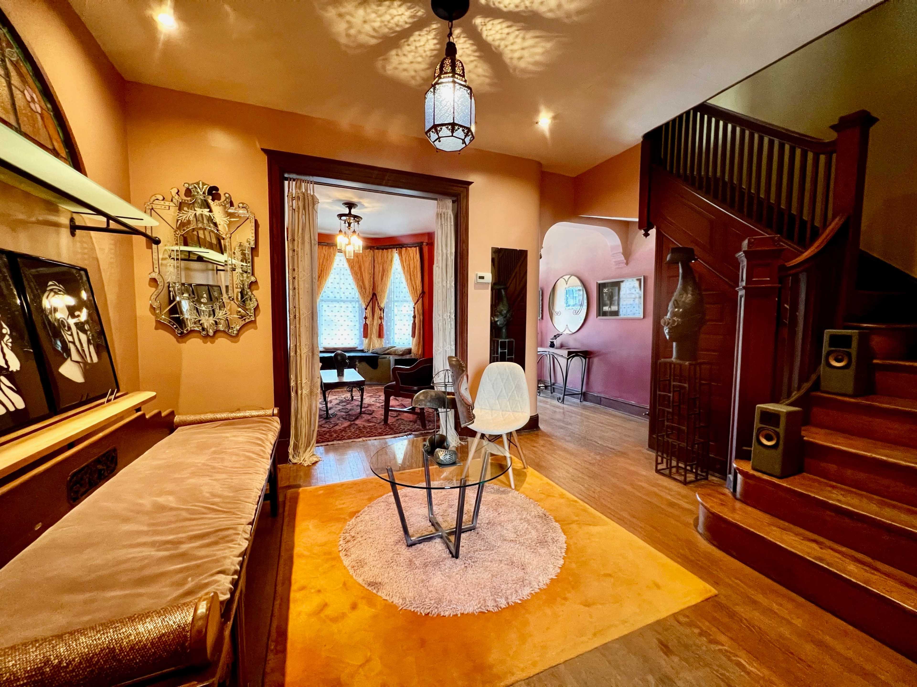 A well-designed entryway leading into a living area, featuring a staircase, decorative lighting, and various pieces of furniture.