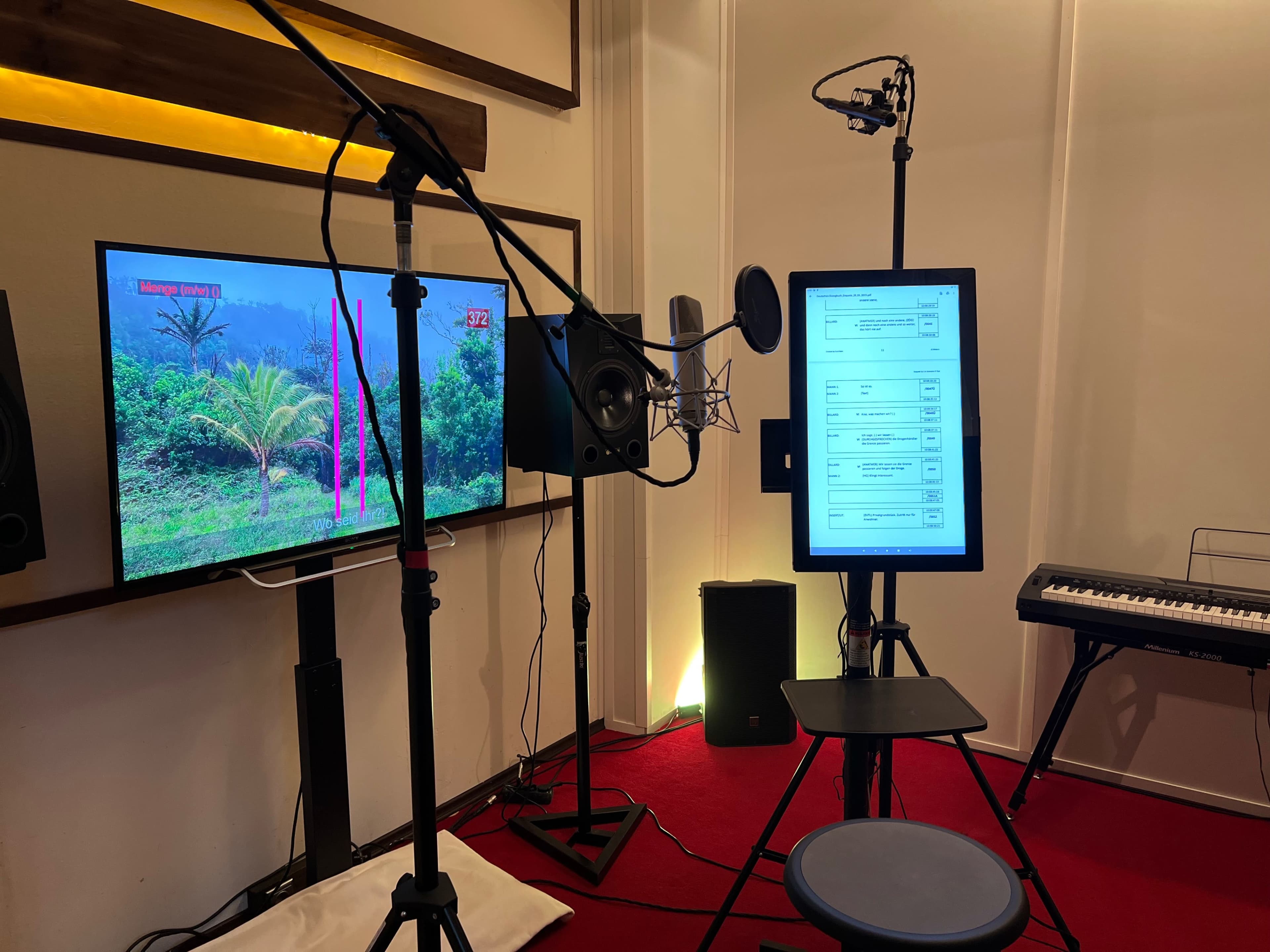 A recording studio setup with a microphone, a monitor displaying a landscape, a tablet on a stand, and a keyboard in the background.