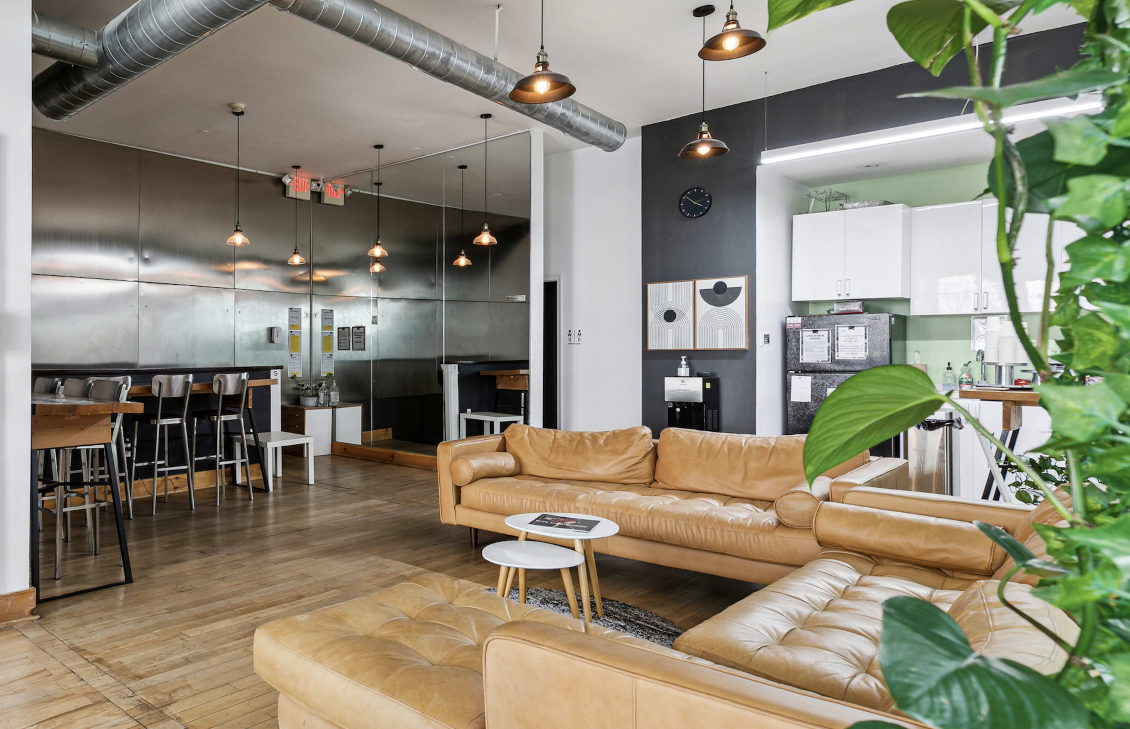 The image shows a modern, open-concept living space with a leather sofa, a small side table, and a dining area featuring high stools and metal accents.