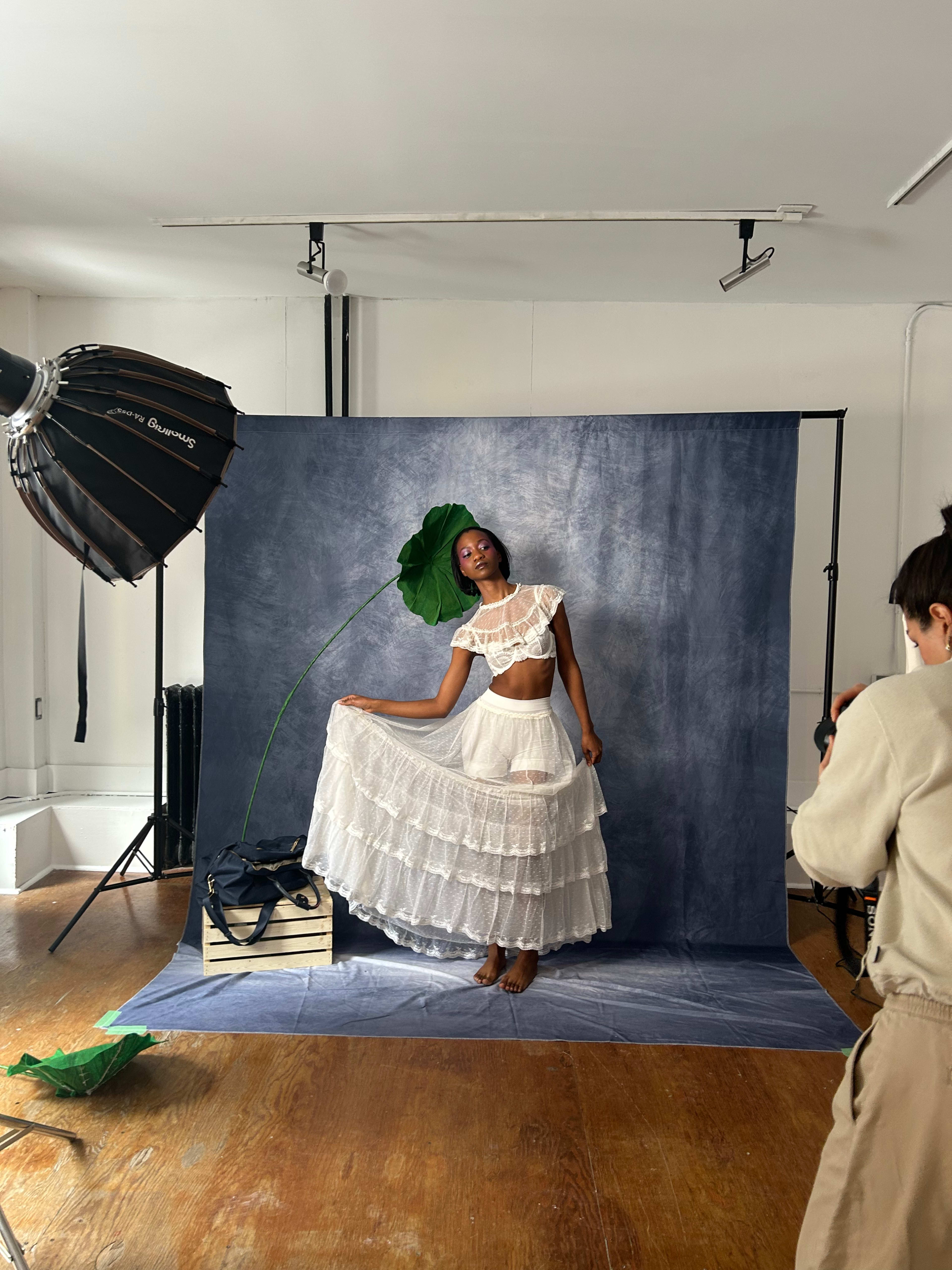 A model poses with a large leaf while standing on a backdrop in a photography studio.