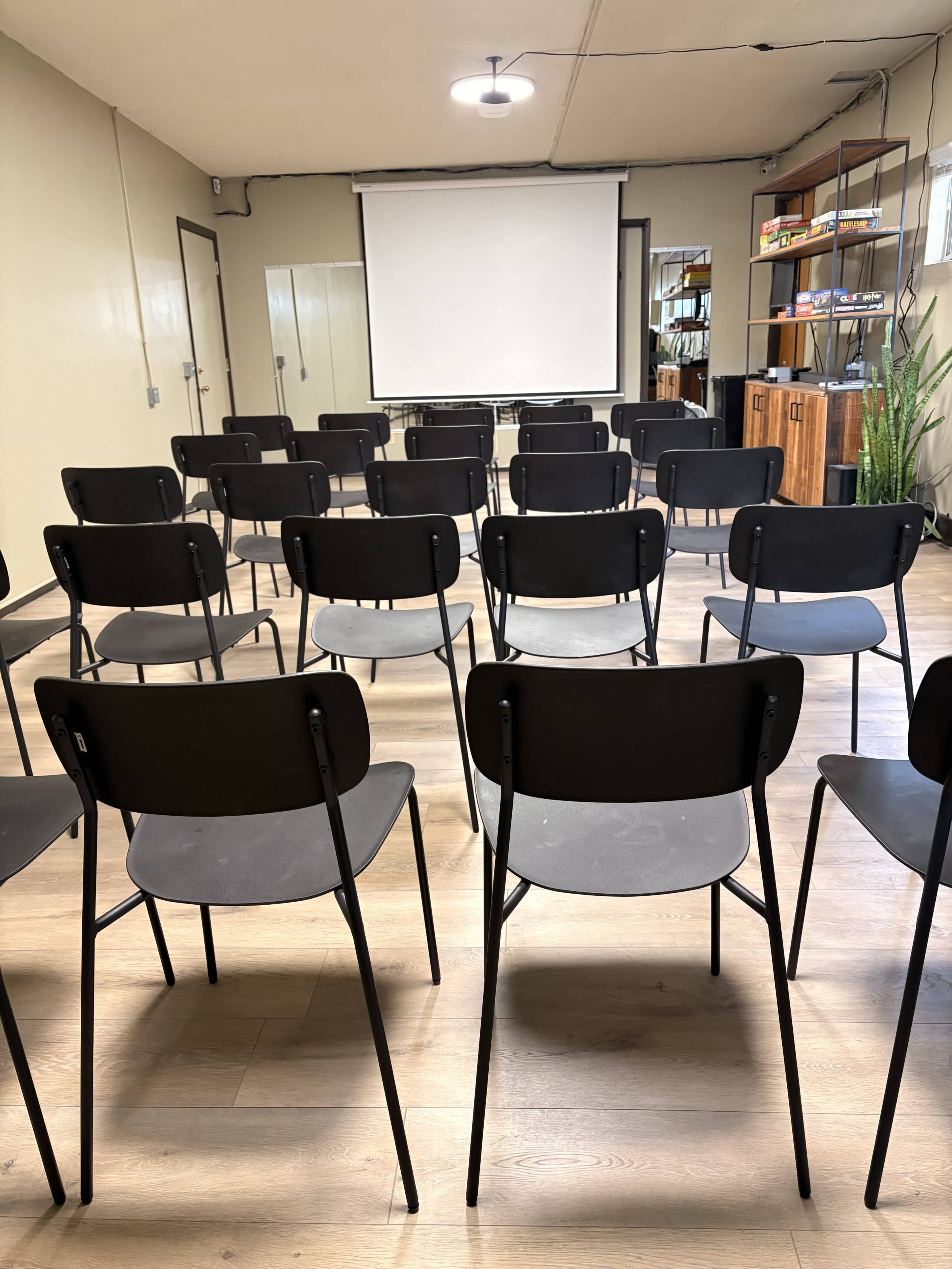 The image shows a seminar room set up with rows of black chairs facing a blank projector screen.