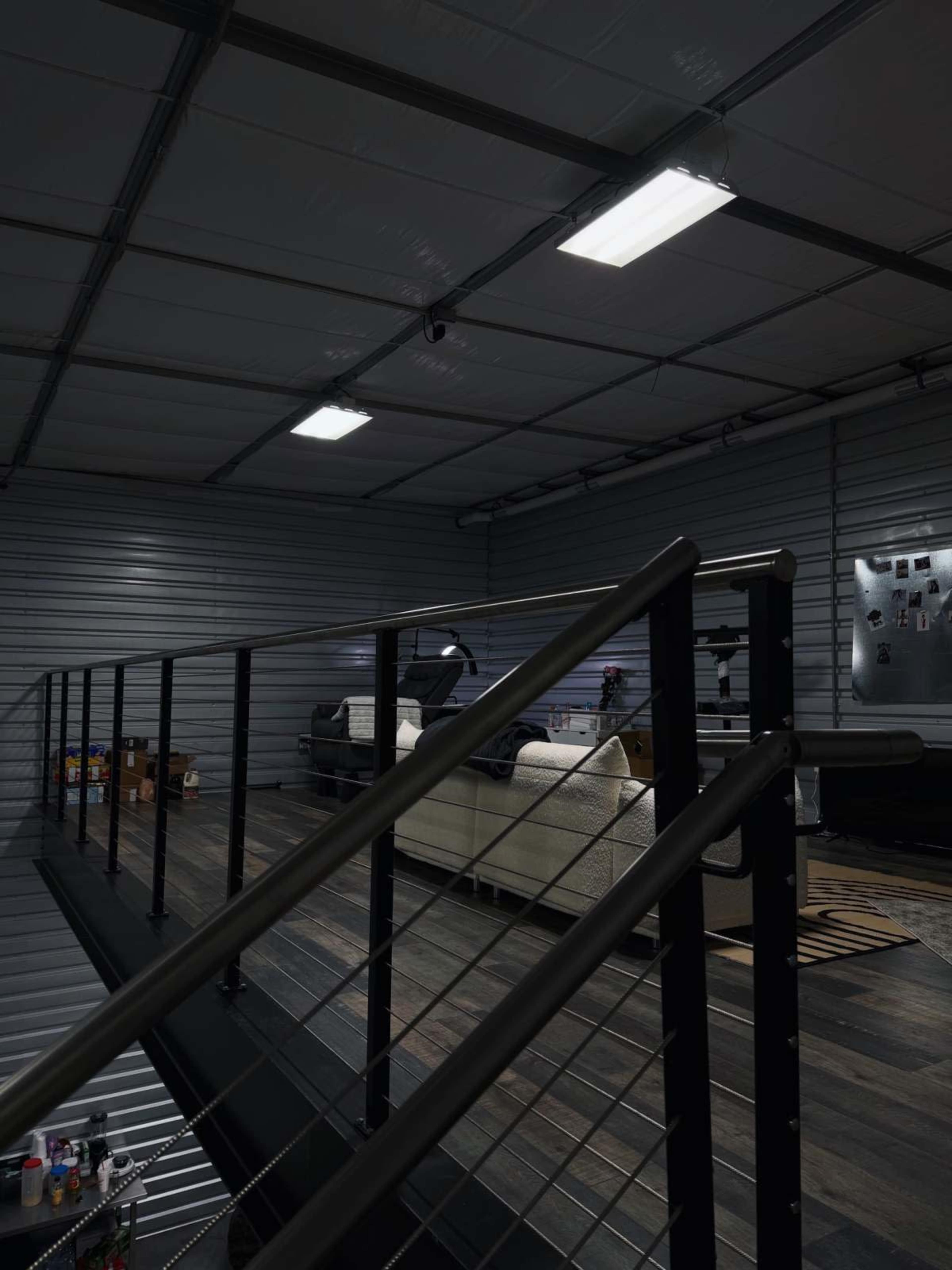 The image shows a modern interior of a warehouse-style space featuring a staircase railing and a cozy seating area visible in the background.