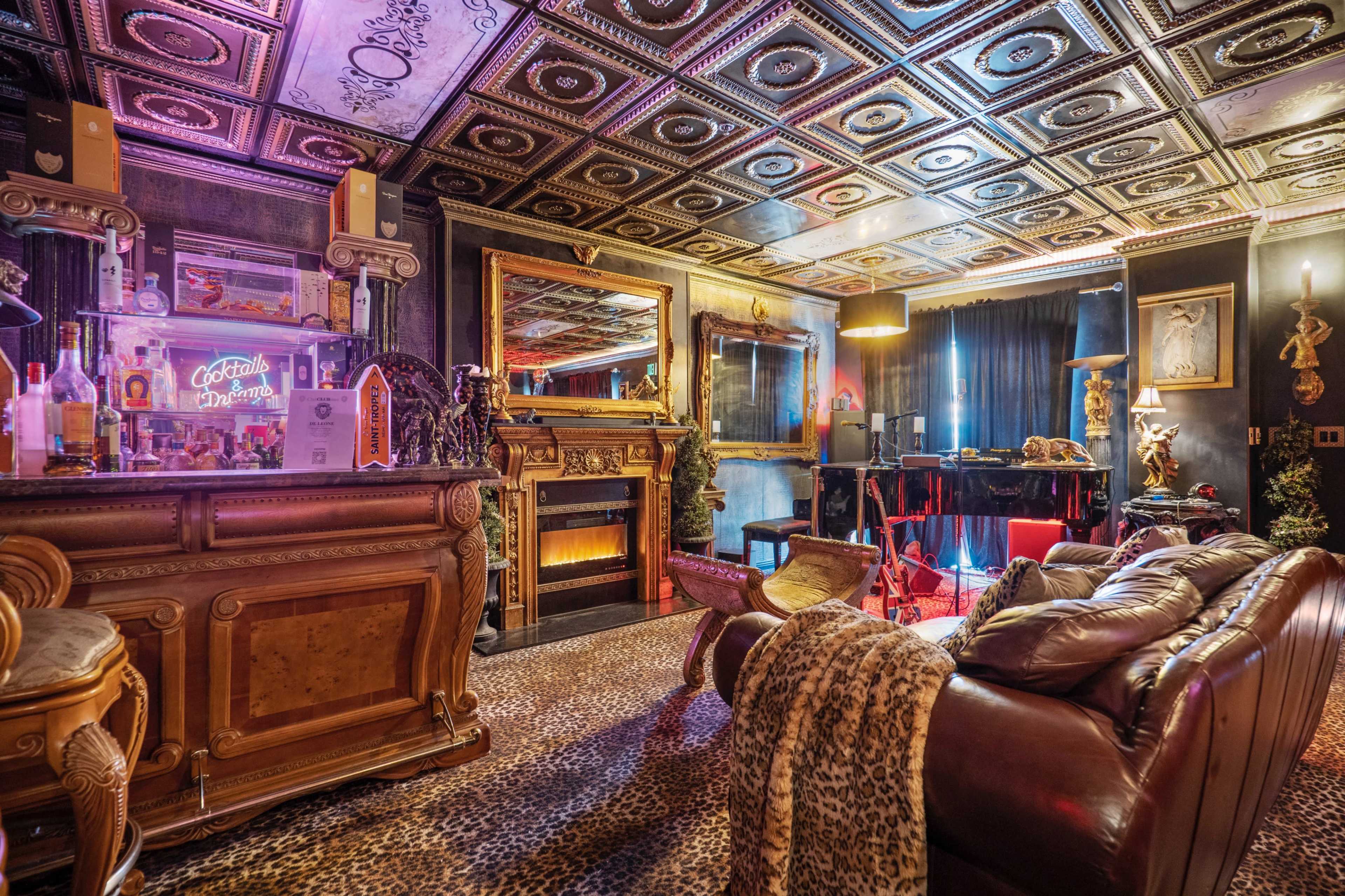 A lavishly decorated lounge area featuring a bar, a fireplace, and ornate ceiling tiles, set against a backdrop of dark walls and animal print decor.