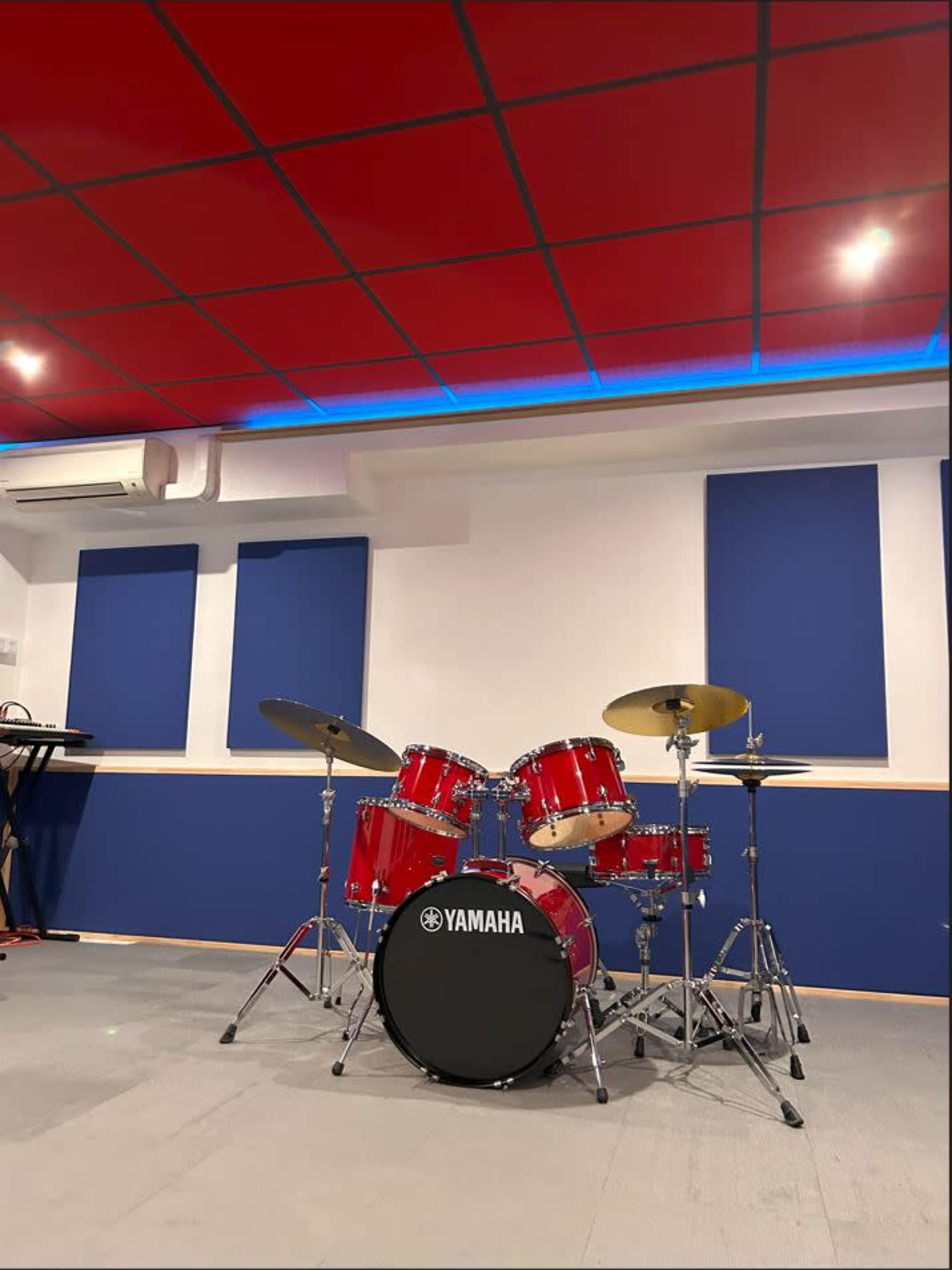 A red drum set placed in a music studio with blue acoustic panels on the walls and a red ceiling.