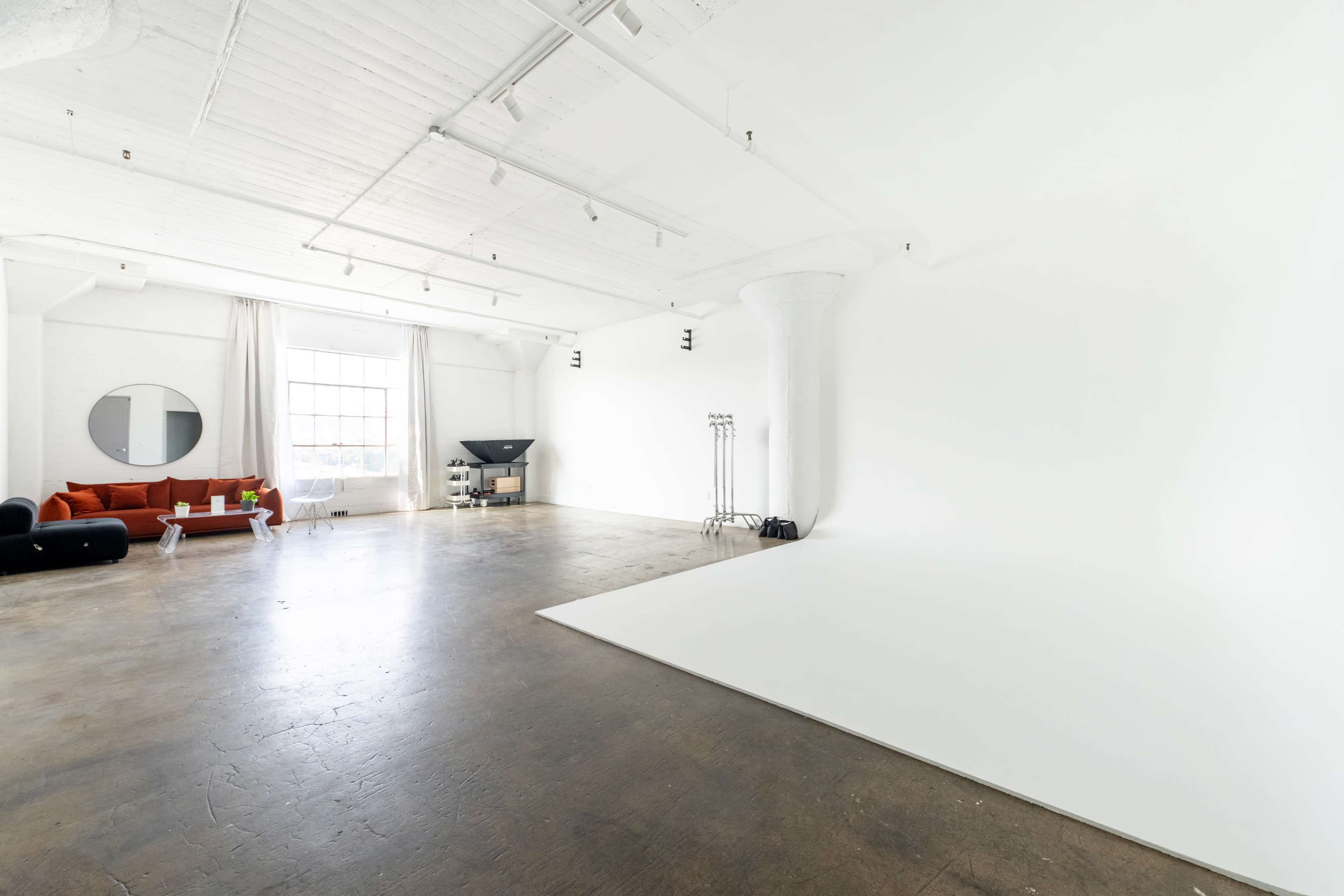 A spacious, modern studio features a white backdrop, polished concrete floor, and minimalist furniture including a red couch.