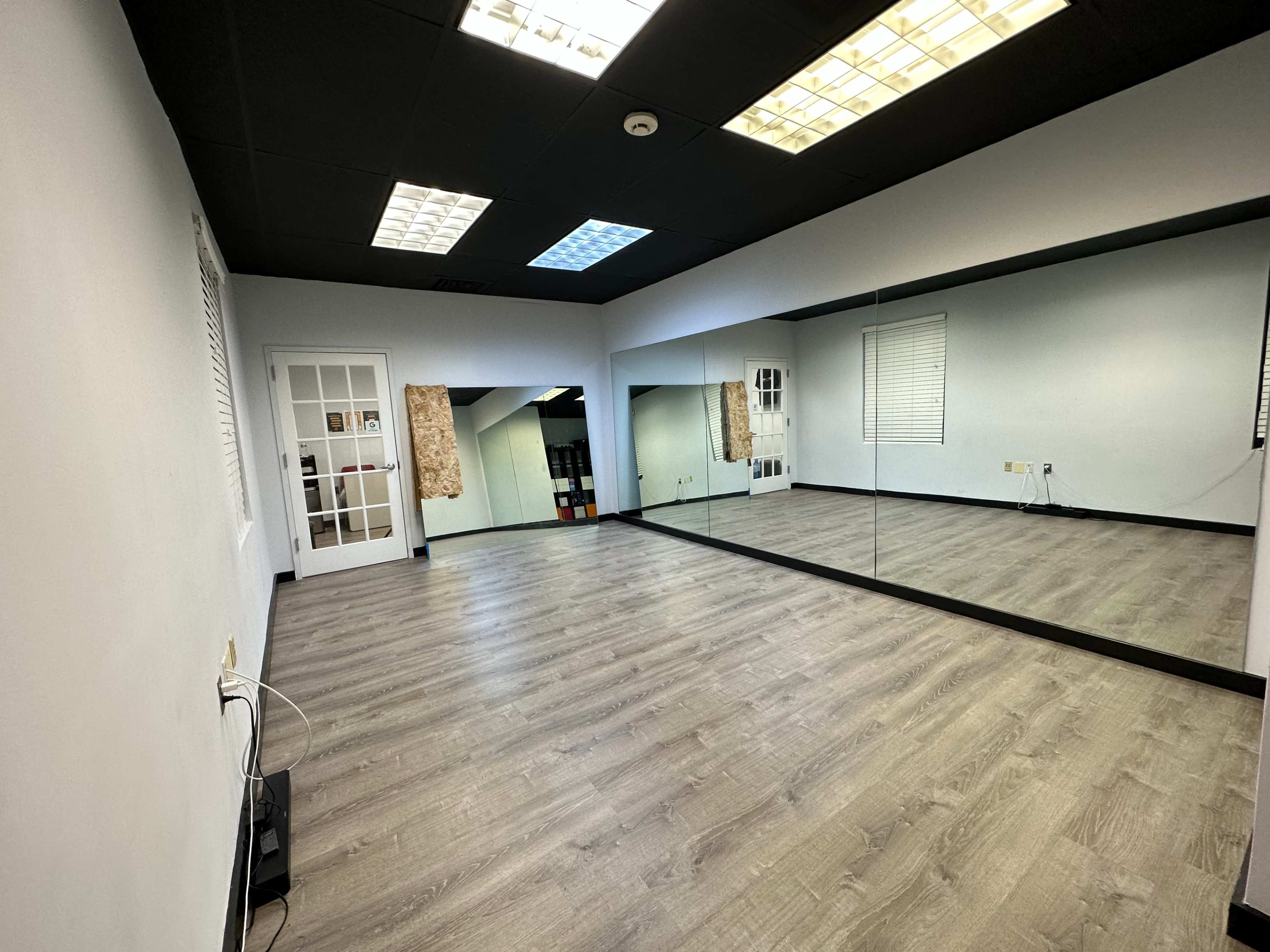 A spacious room with a wooden floor, white walls, a large mirror, and a door leading to another area.