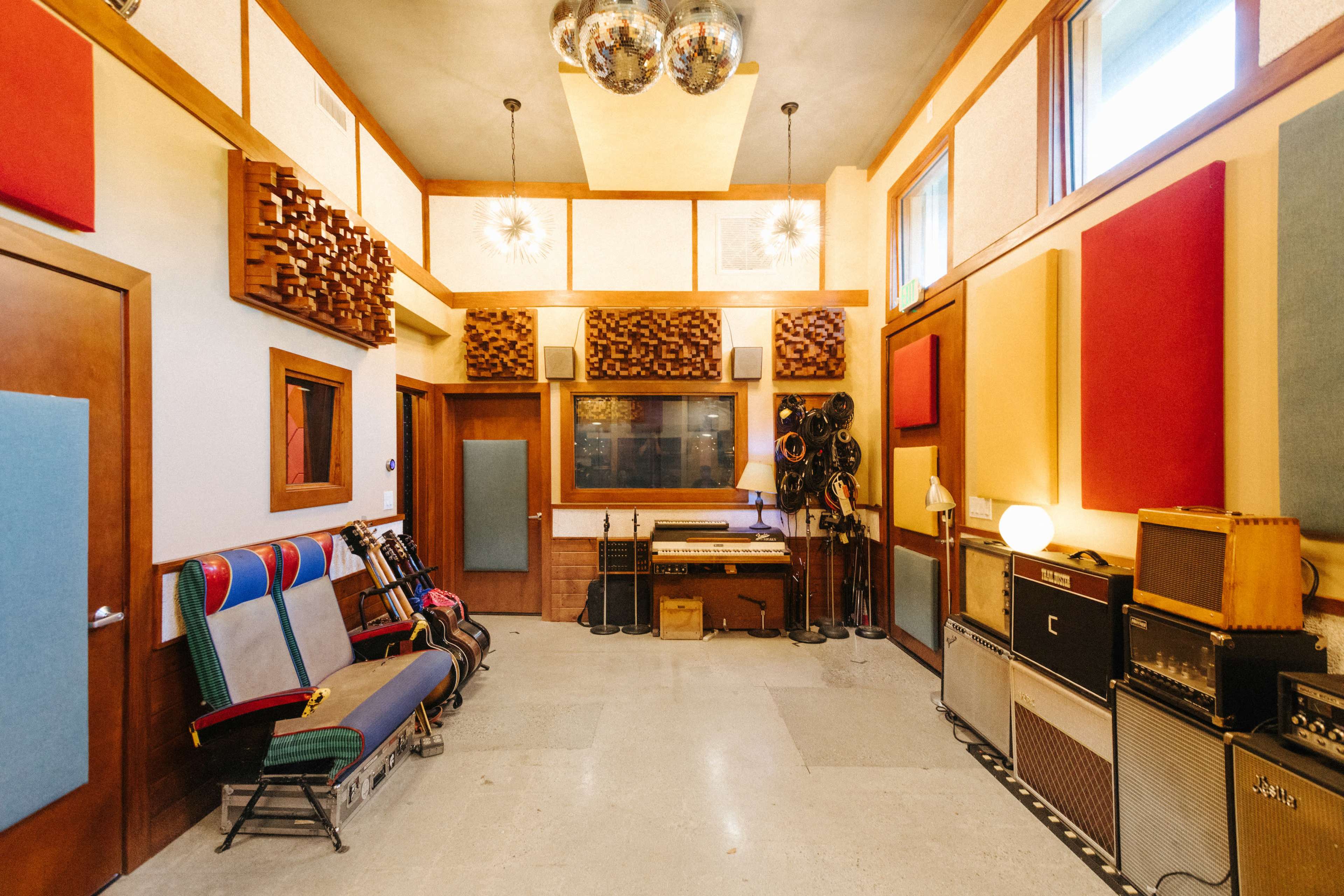 A music recording studio features colorful acoustic panels, vintage amplifiers, and guitars arranged along the walls.