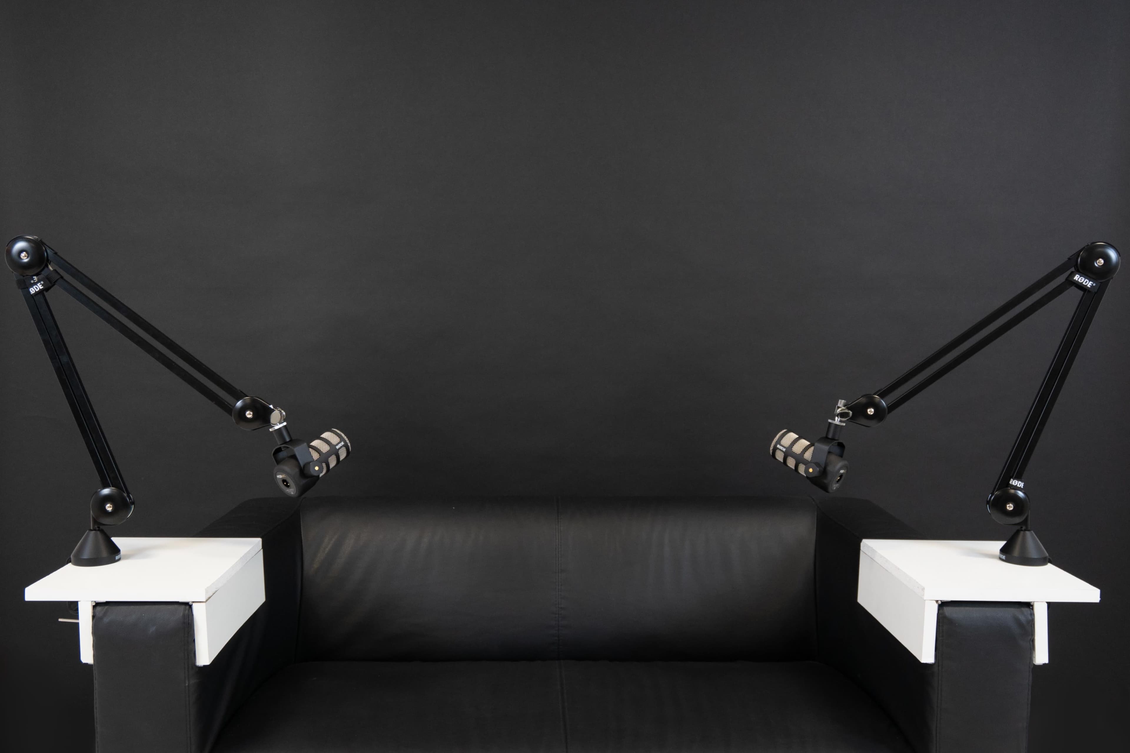 A black couch with two adjustable microphone stands mounted on white platforms at each end.