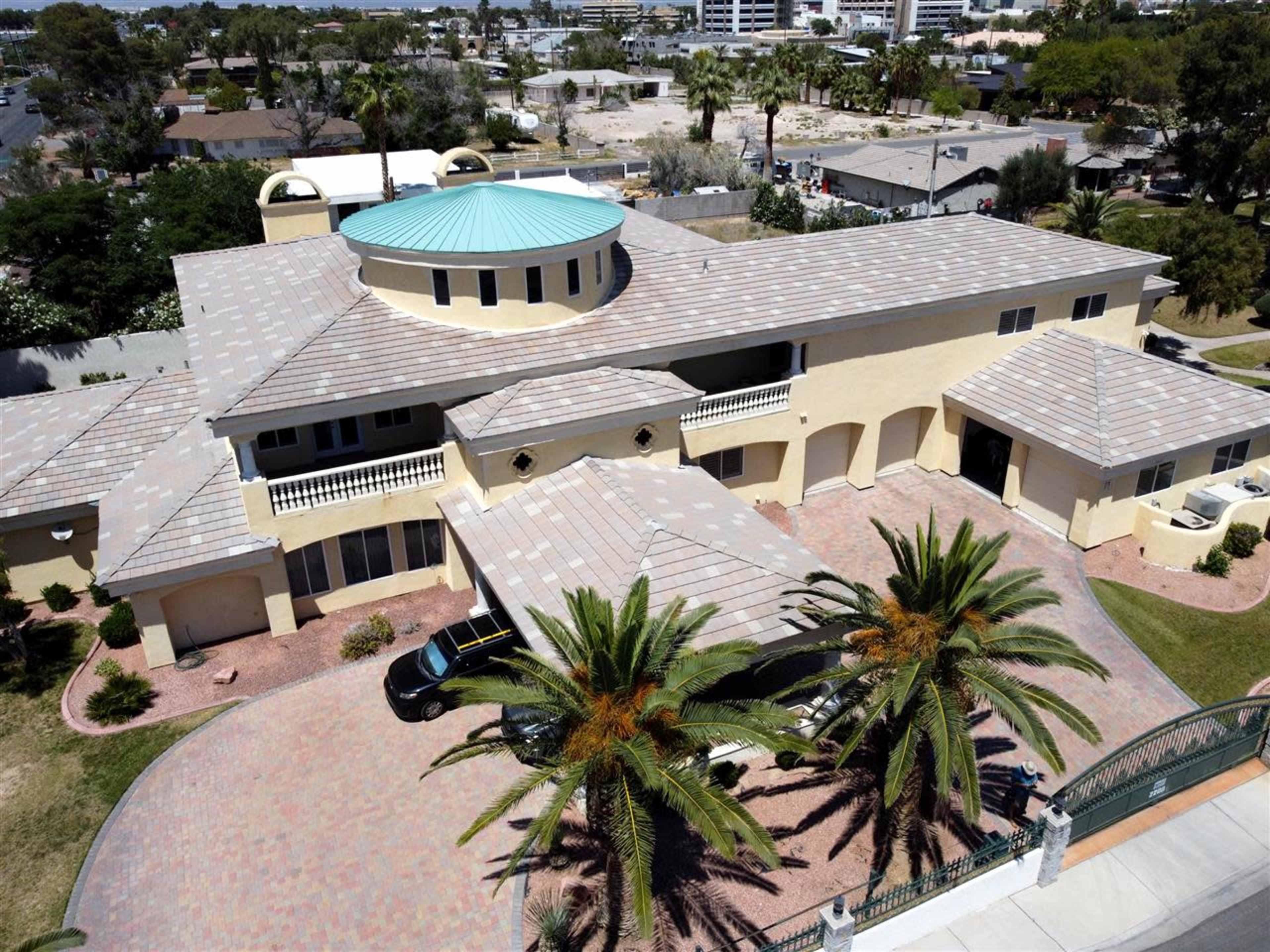 A large, two-story house with a circular roof section and palm trees in the landscaped front yard.
