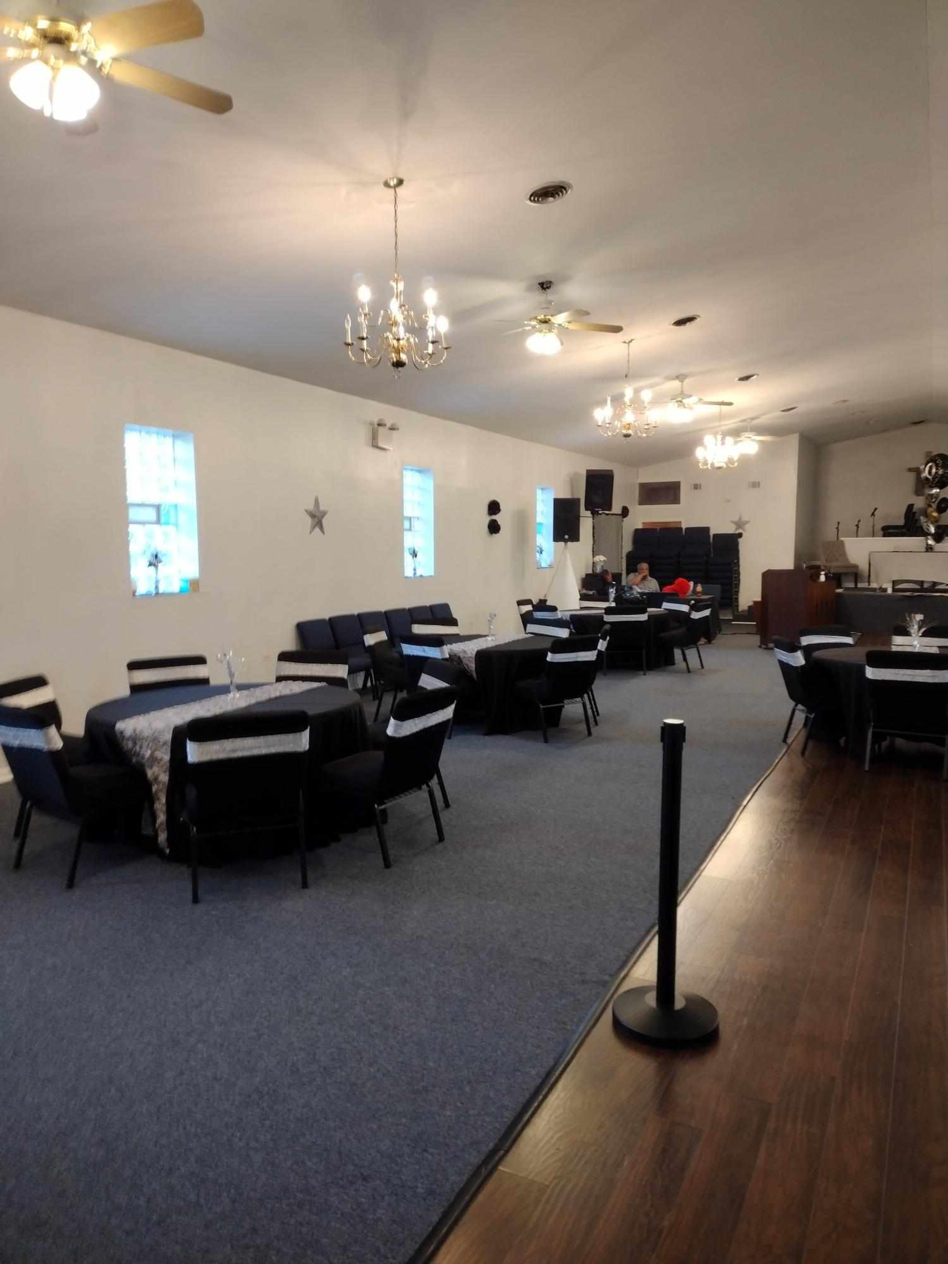 An indoor event space with tables set for dining, chairs arranged, and chandeliers hanging from the ceiling.