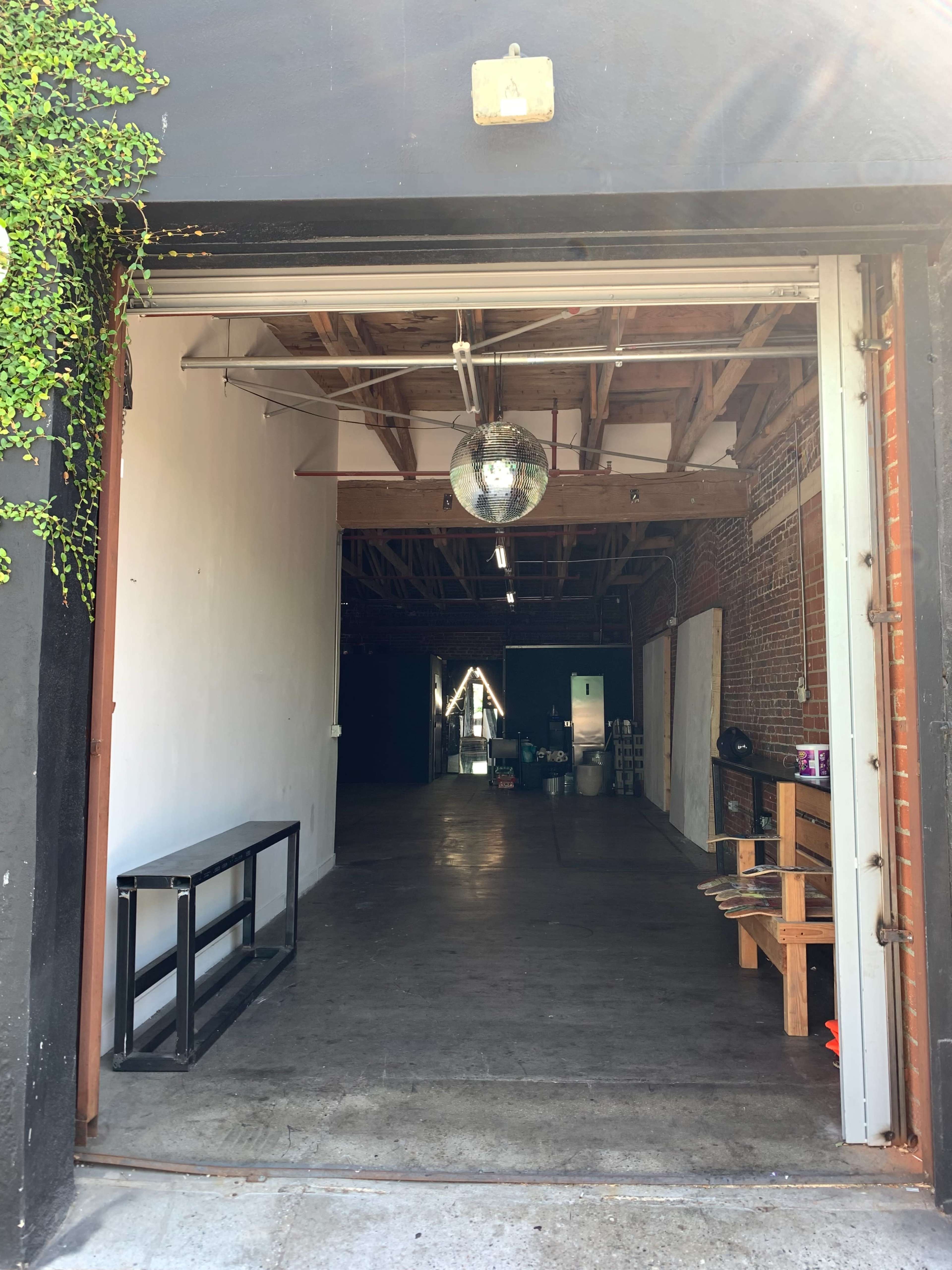 An open doorway leading into a spacious, industrial-style interior with exposed brick walls and a discoball hanging from the ceiling.