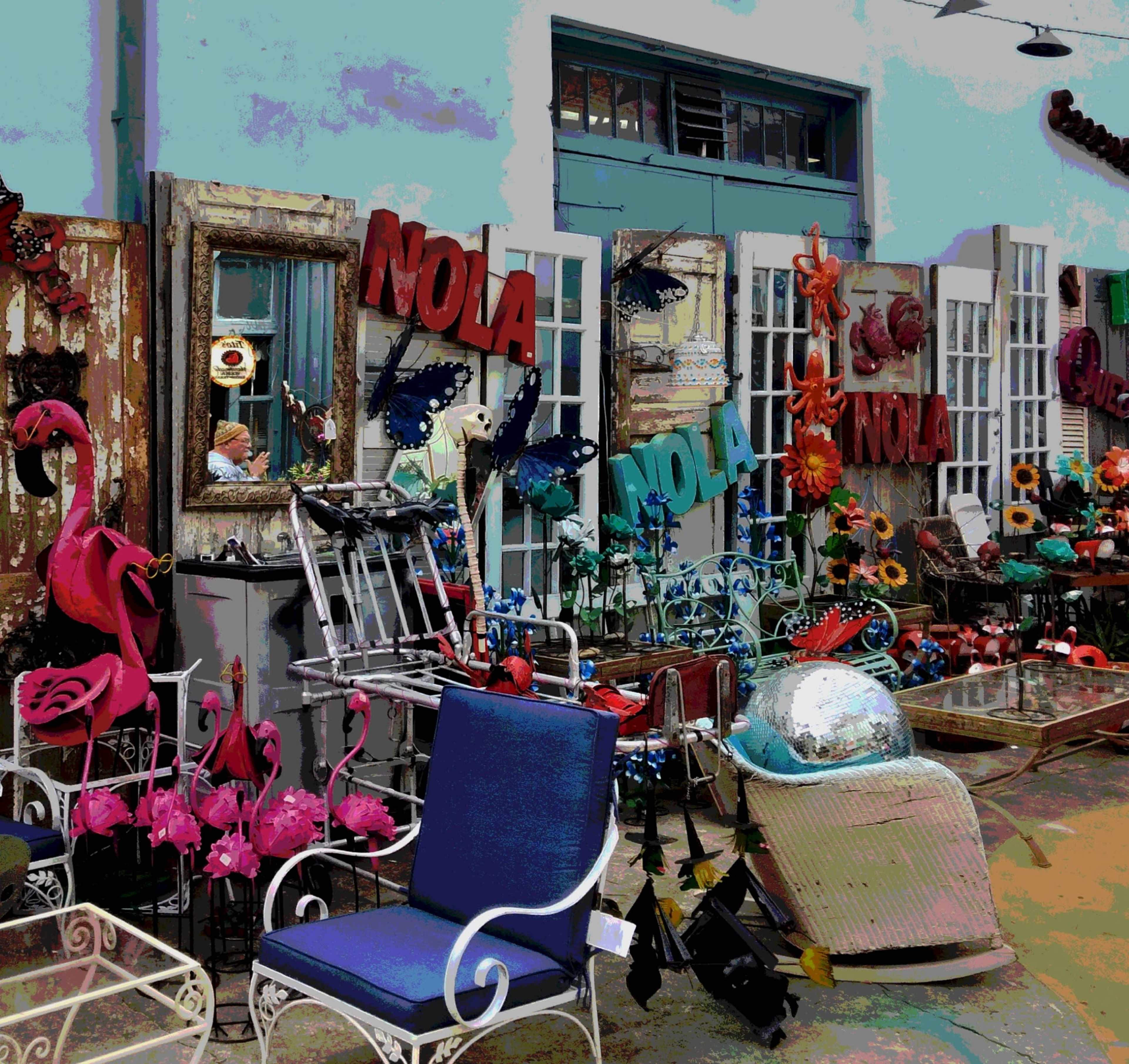 The image shows a colorful display of various decorative items and furniture, including flamingo sculptures, chairs, and vibrant signs that read "NOLA."