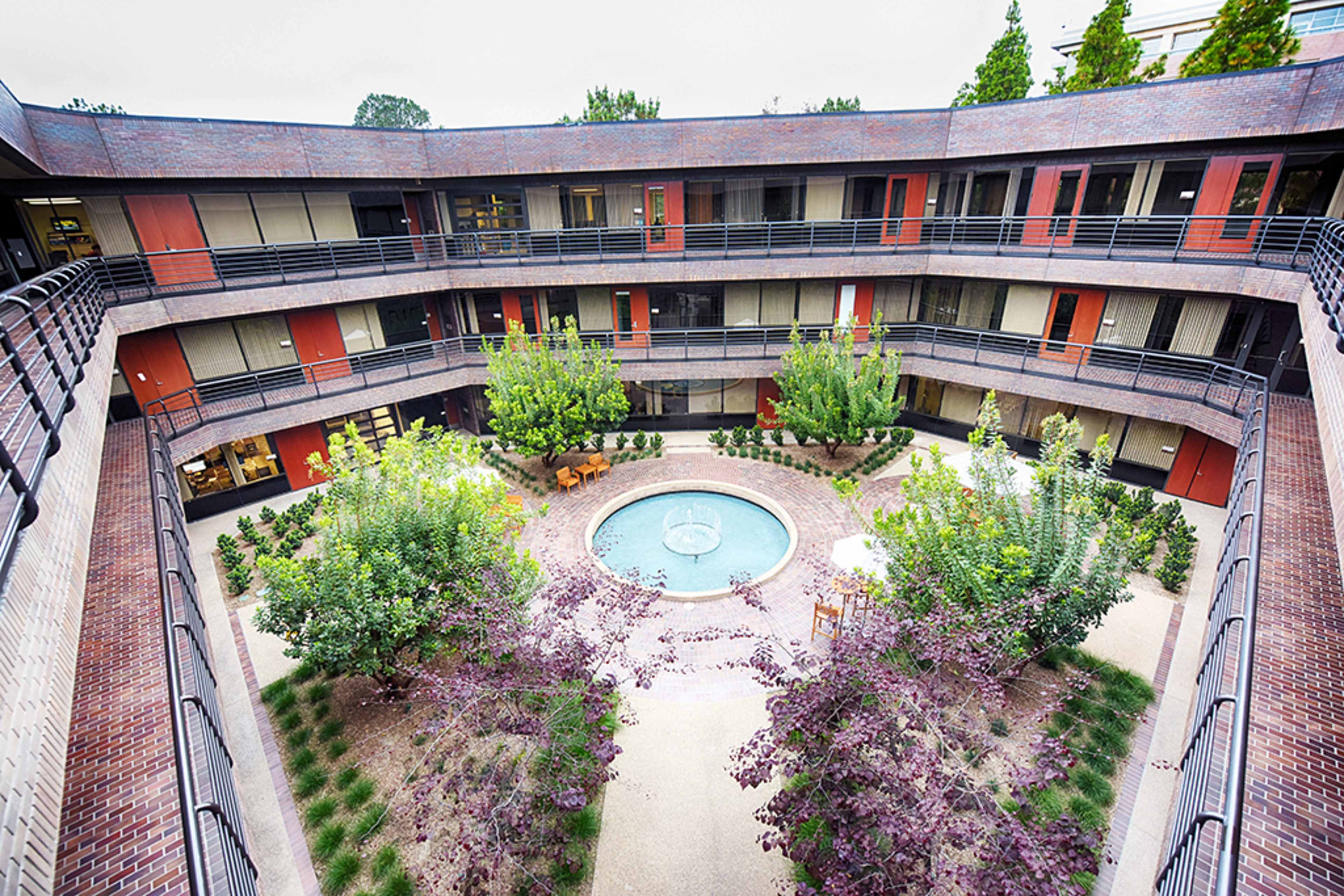 A circular courtyard surrounded by a multi-level building, featuring a central fountain and landscaped trees and plants.