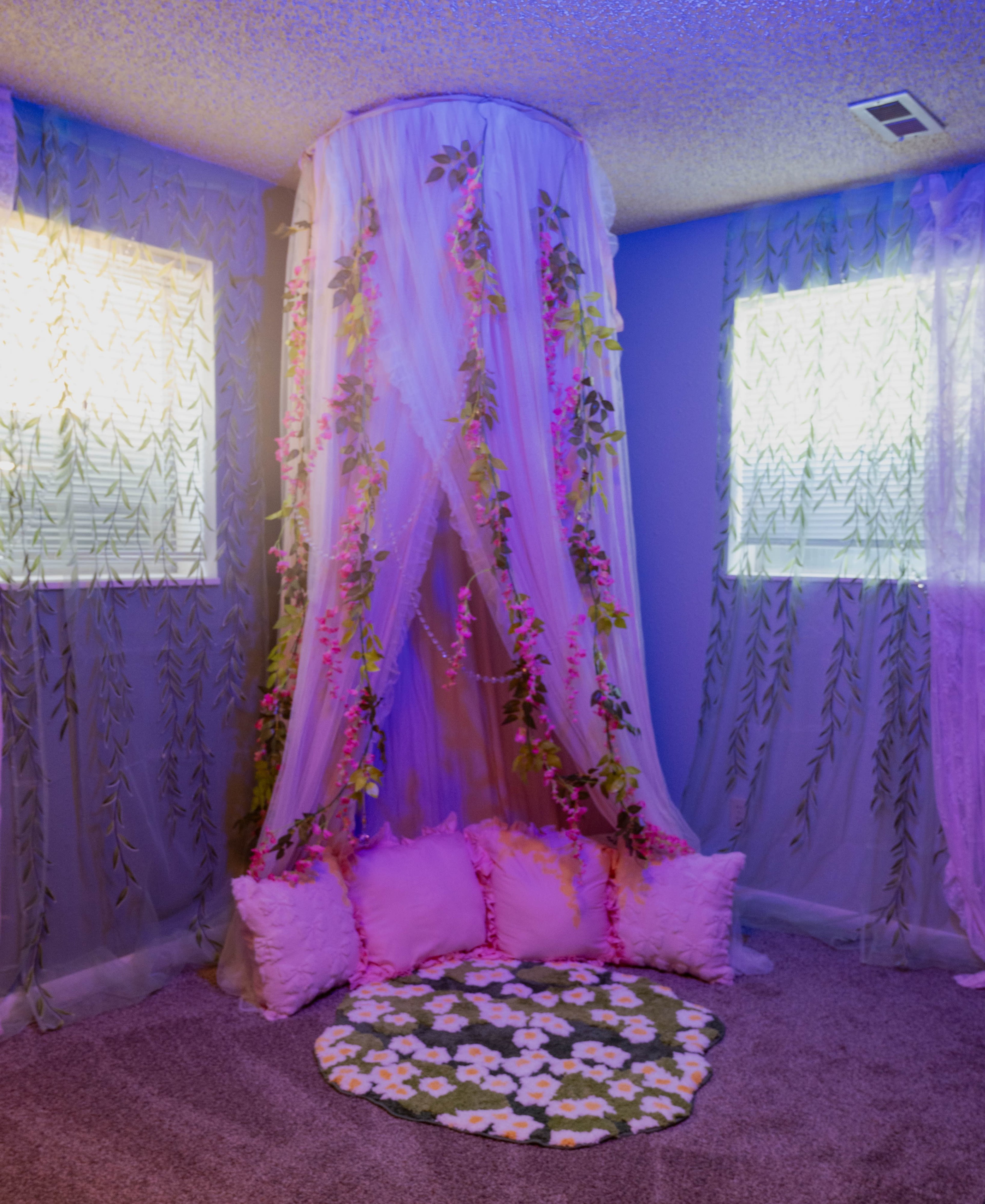 A cozy corner in a room features a plush seating area surrounded by flowing sheer curtains adorned with greenery and floral decorations.