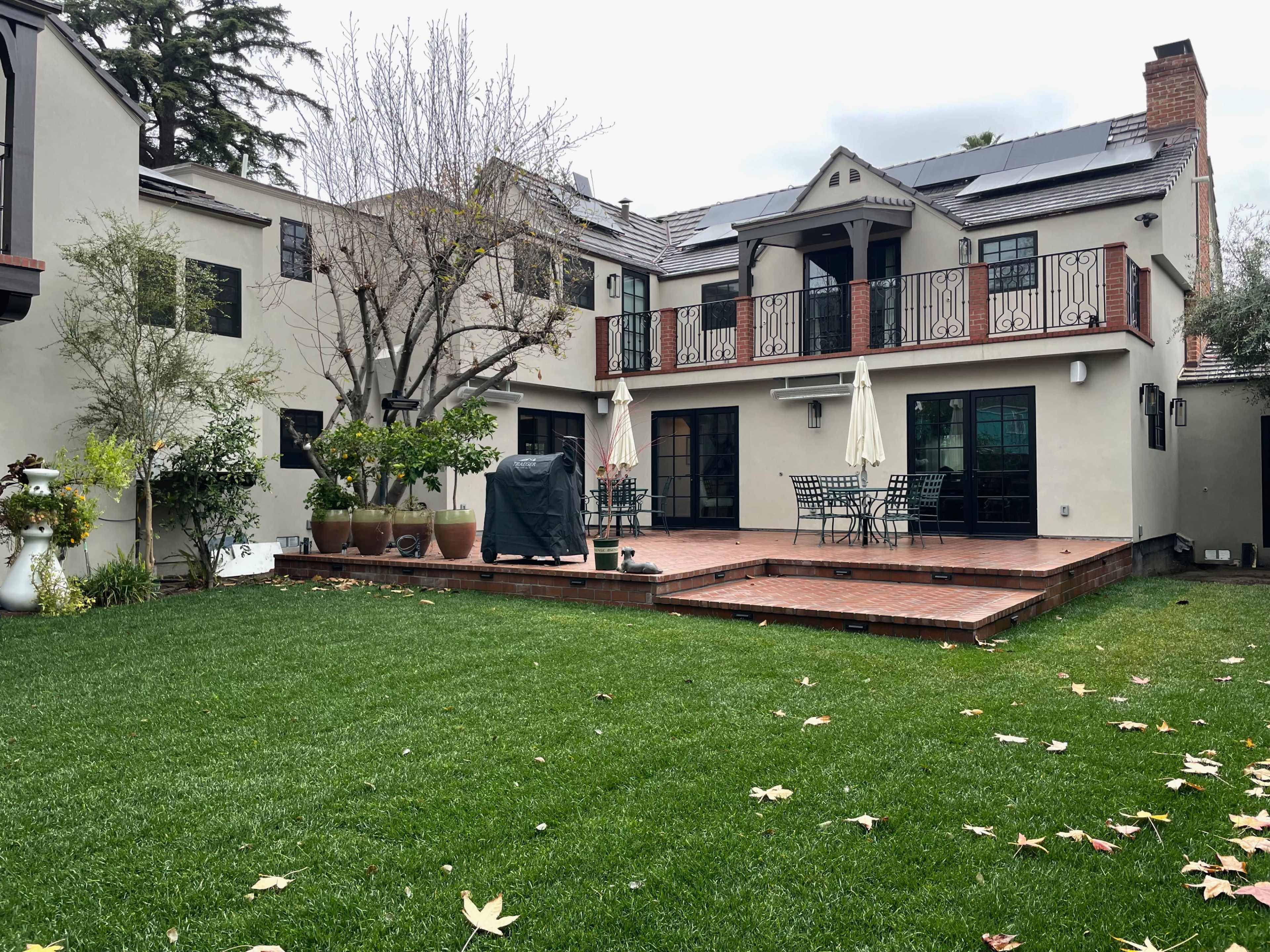 A backyard with a green lawn, a wooden deck with dining furniture, and an adjacent house featuring large windows and a balcony.
