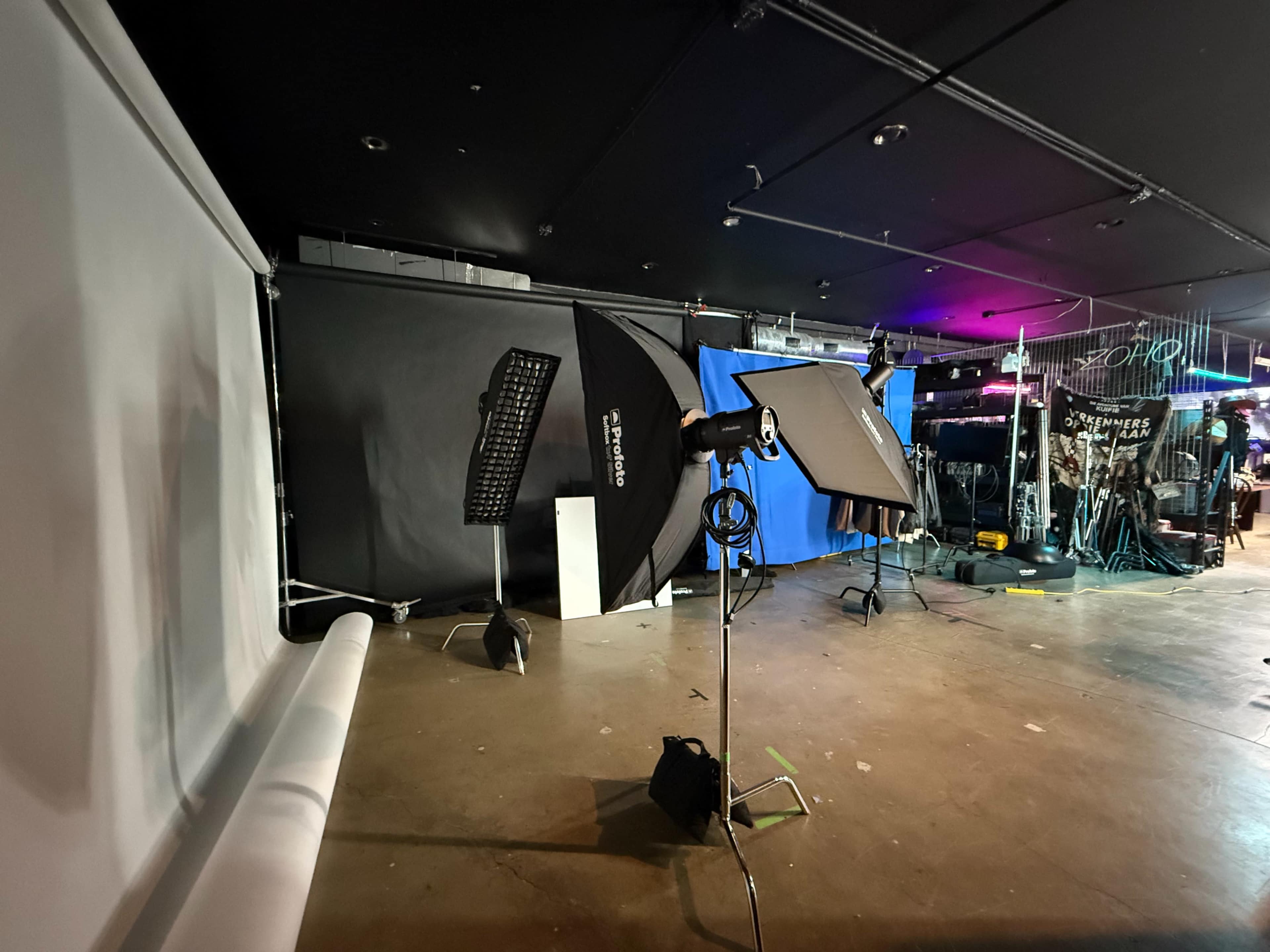 The image shows a photography studio setup with various backdrops, lighting equipment, and a blank roll of paper on the floor.