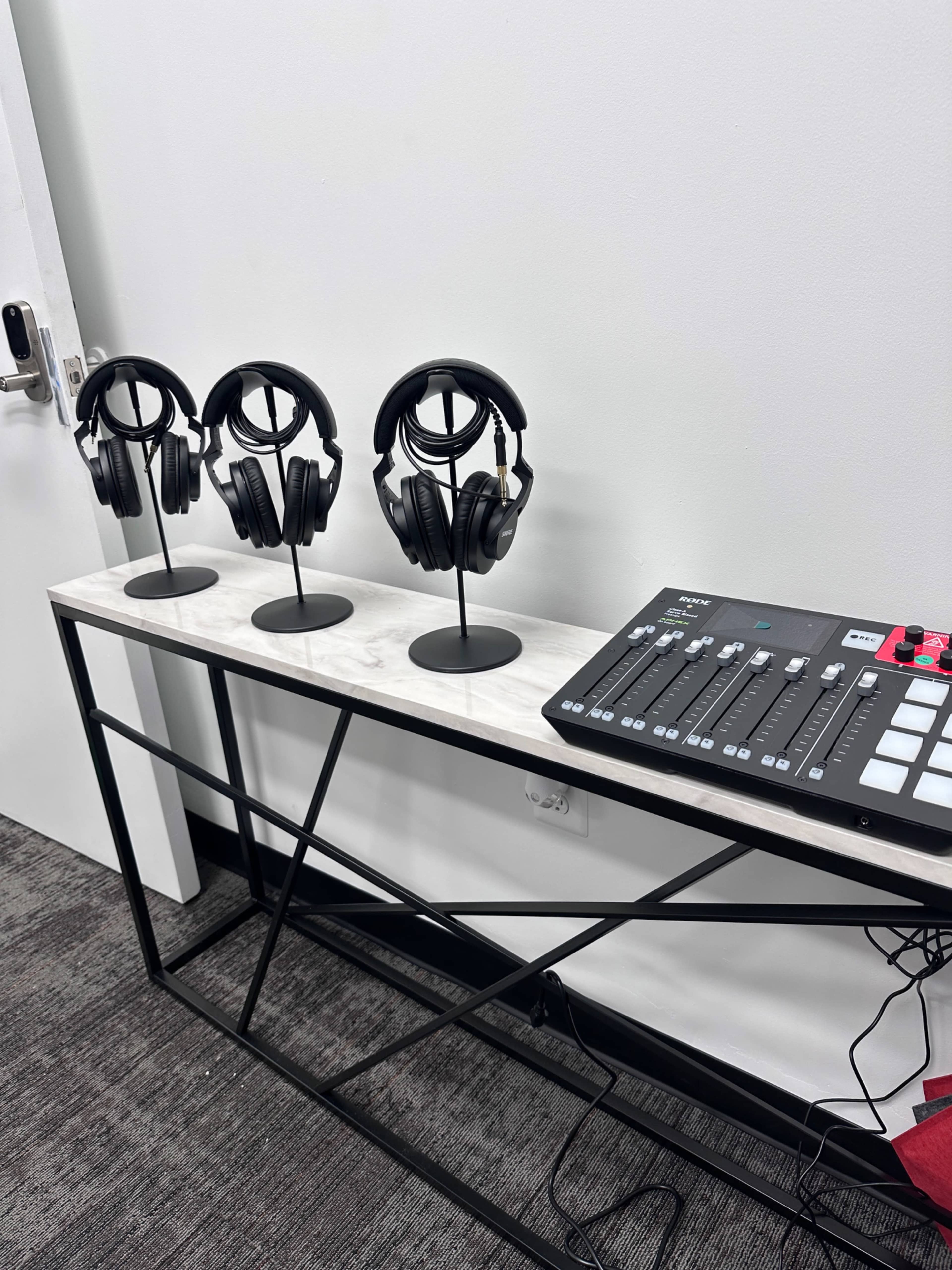 Three pairs of black headphones are displayed on stands atop a white table next to a control panel with buttons and sliders.