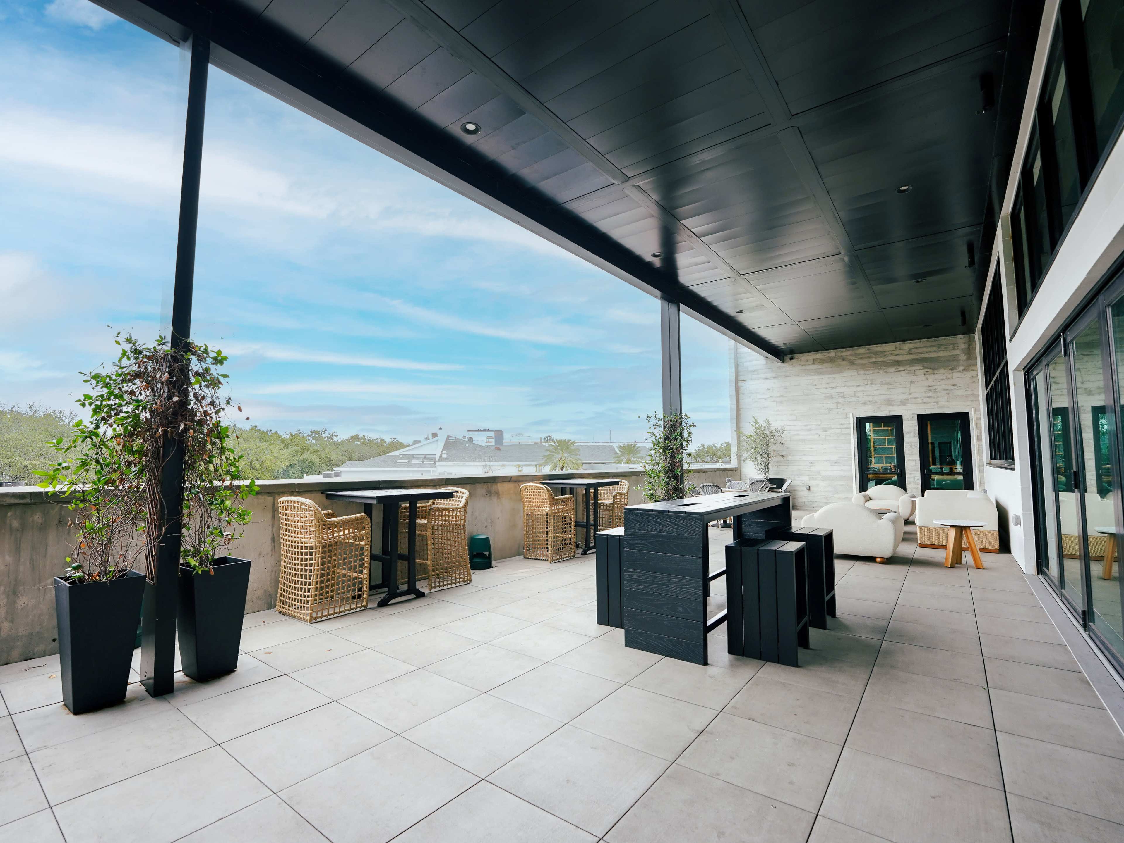 The image shows a spacious outdoor terrace with modern furniture and planters, overlooking a clear sky.