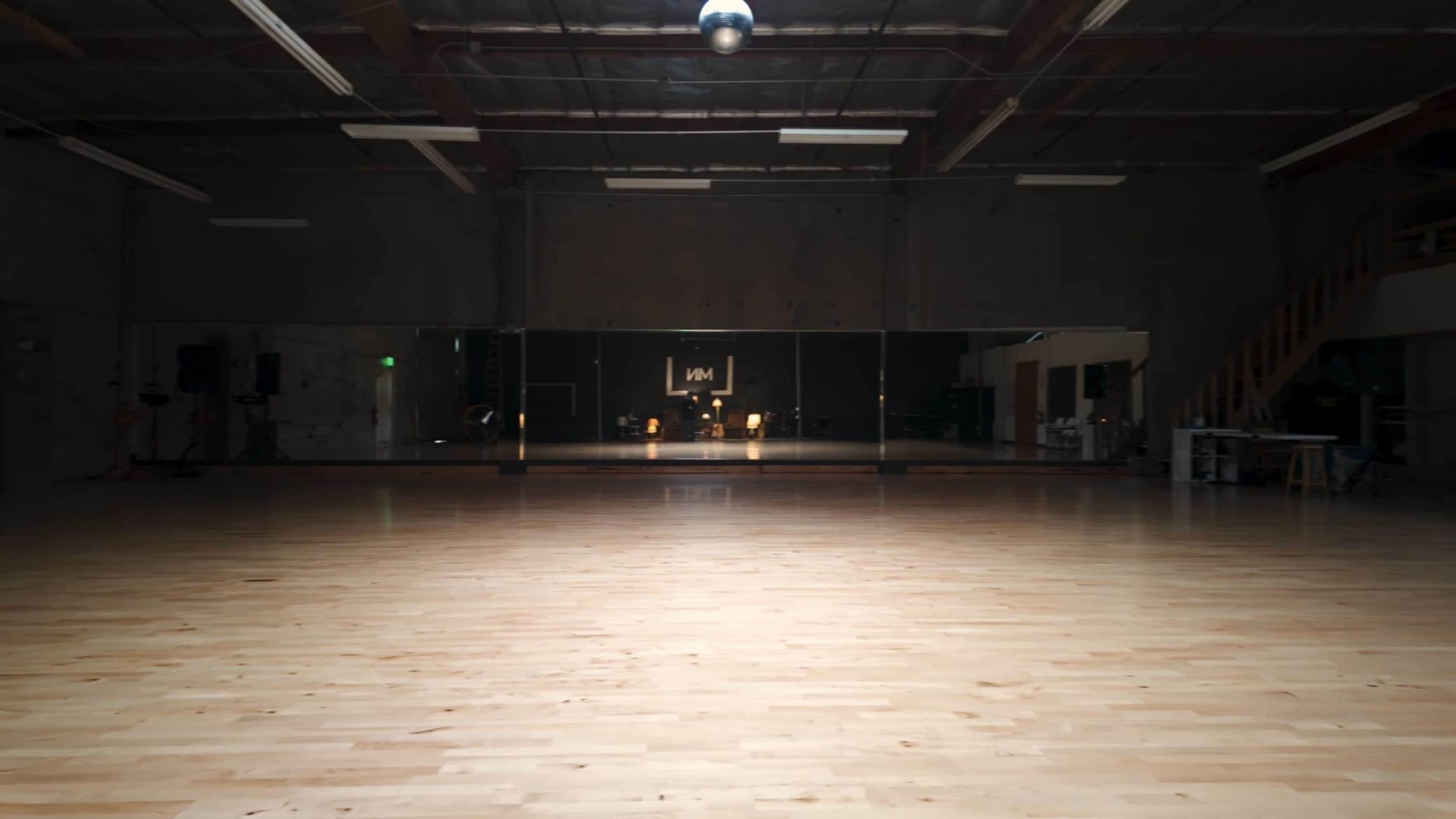 A large, empty dance studio with wooden flooring and mirrored walls under a single overhead light.