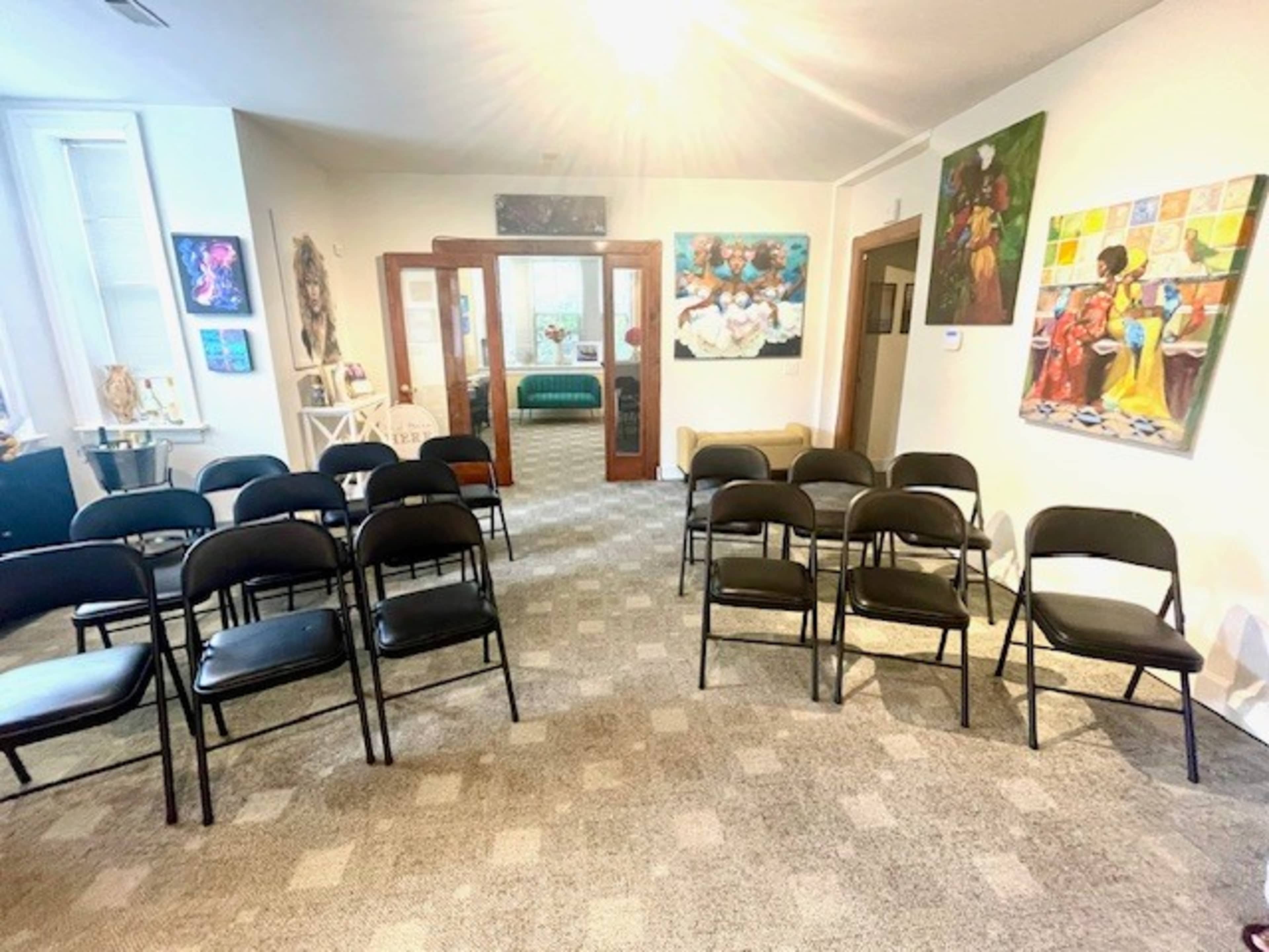 The image shows a meeting room with several black folding chairs arranged in rows, facing a wall adorned with colorful artwork.