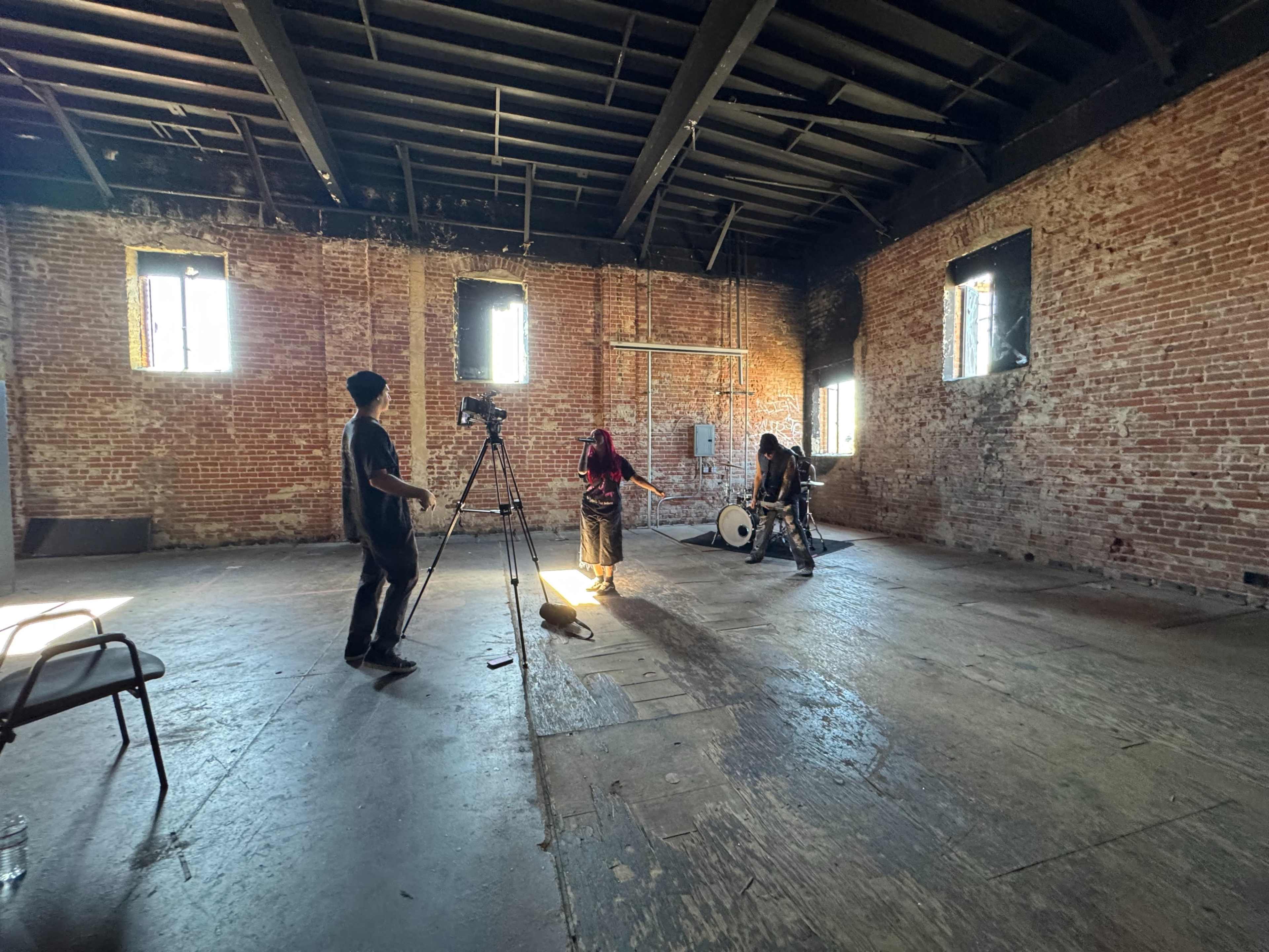 A small group of people sets up equipment in a spacious, brick-walled room with large windows.