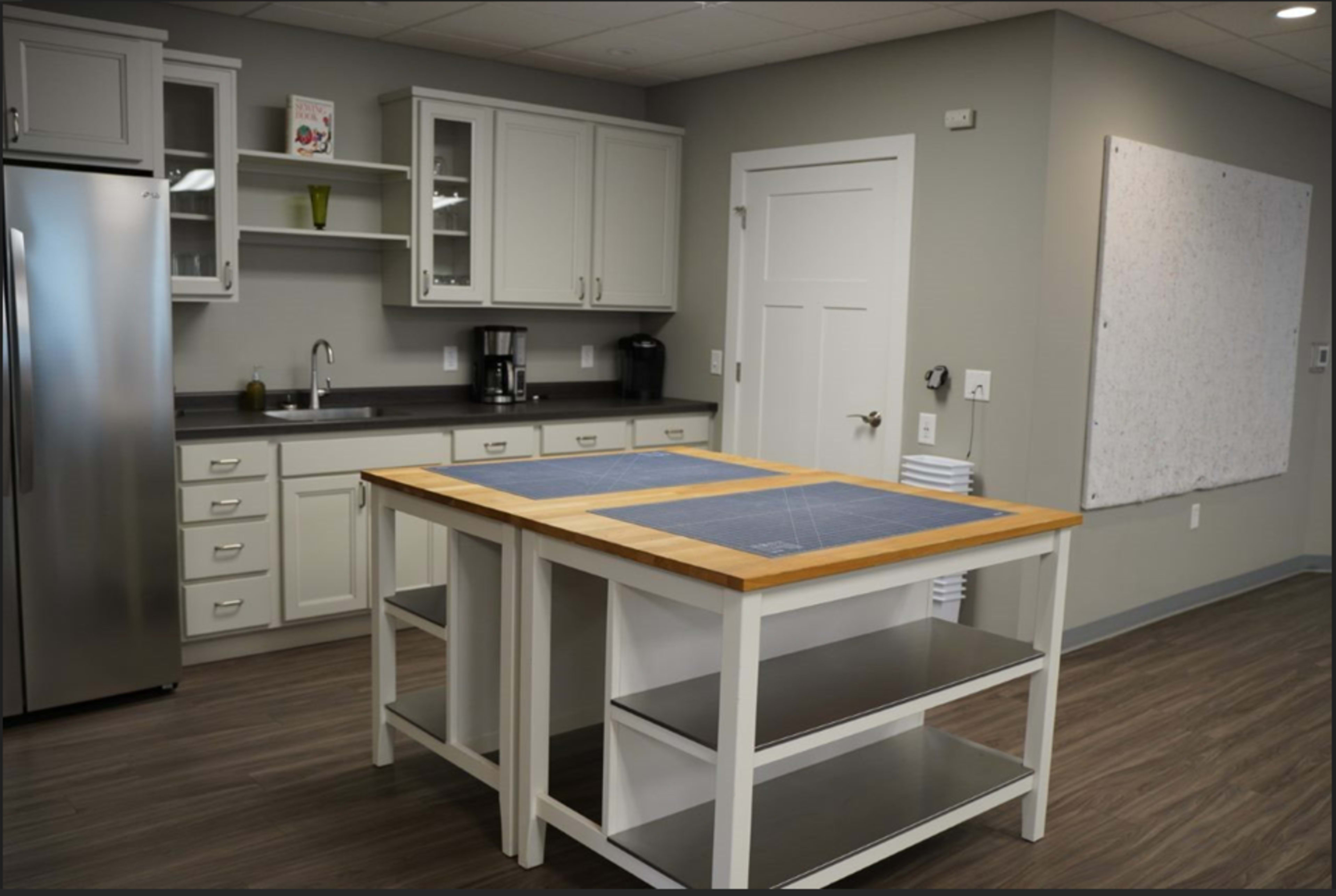 The image shows a modern kitchen with a central island, stainless steel appliances, white cabinets, and gray walls.