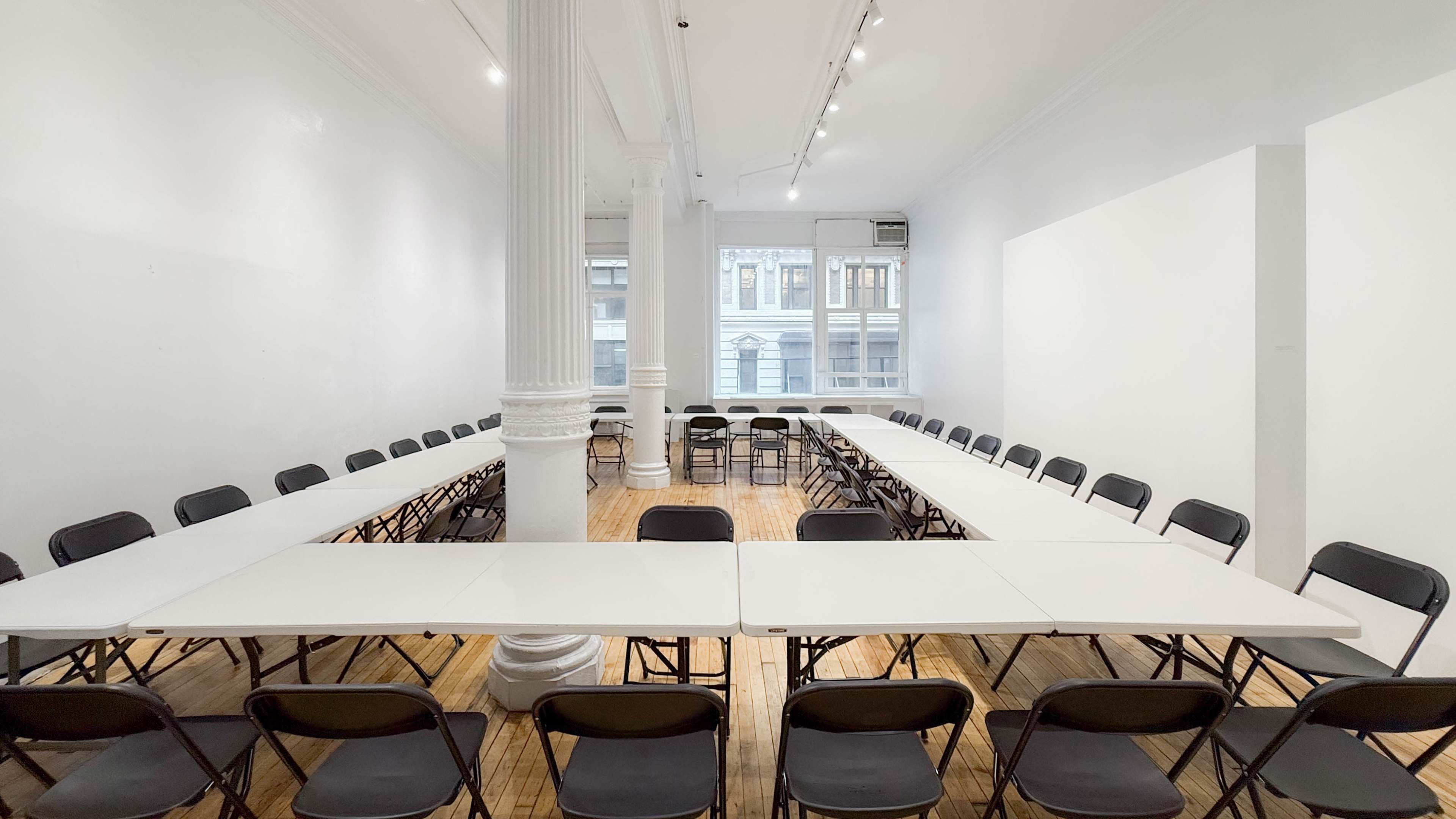 A spacious room features a large arrangement of folding tables and chairs in a U-shape around a central column.