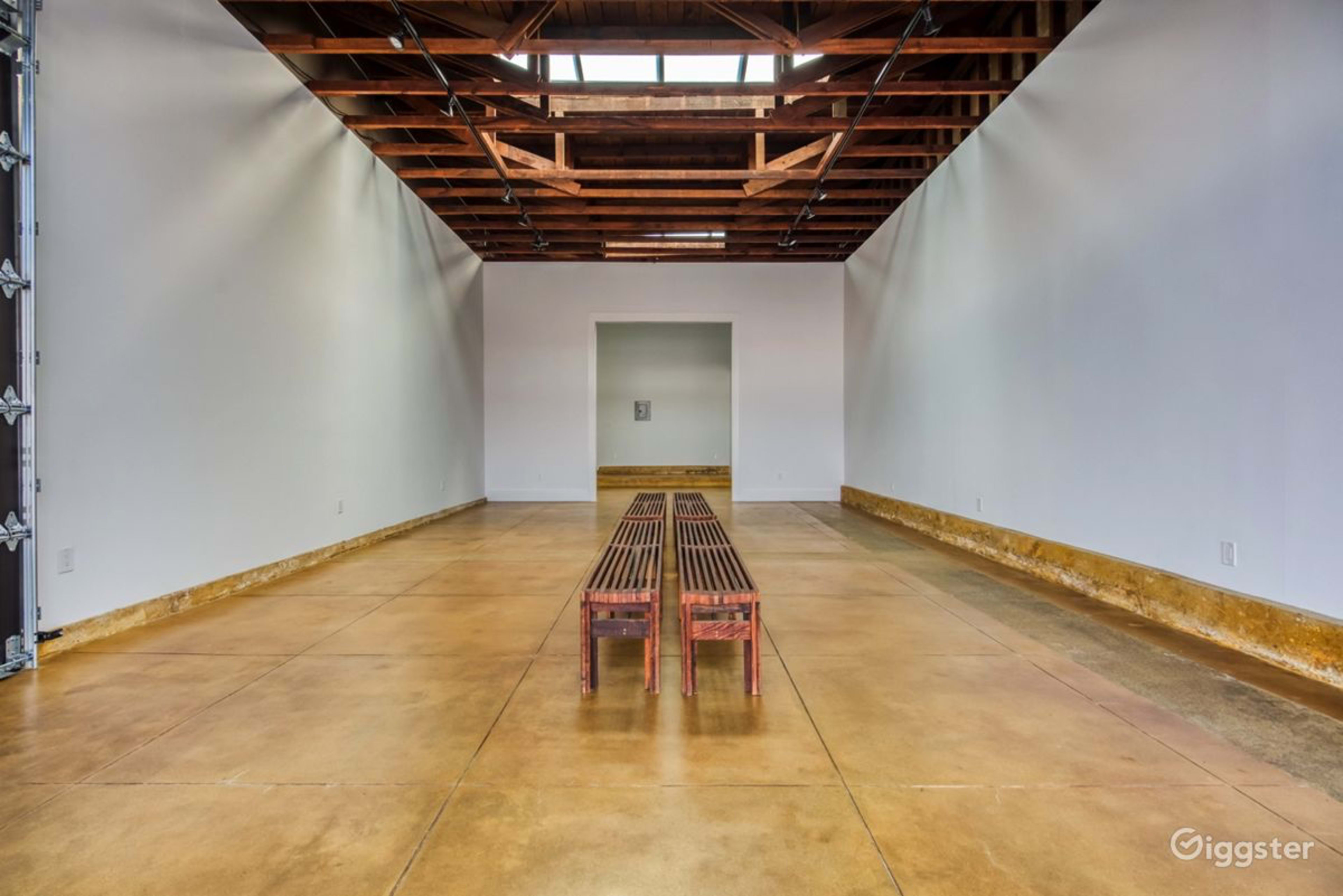 A spacious, empty room with a concrete floor, wooden beams on the ceiling, and a wooden bench in the center.